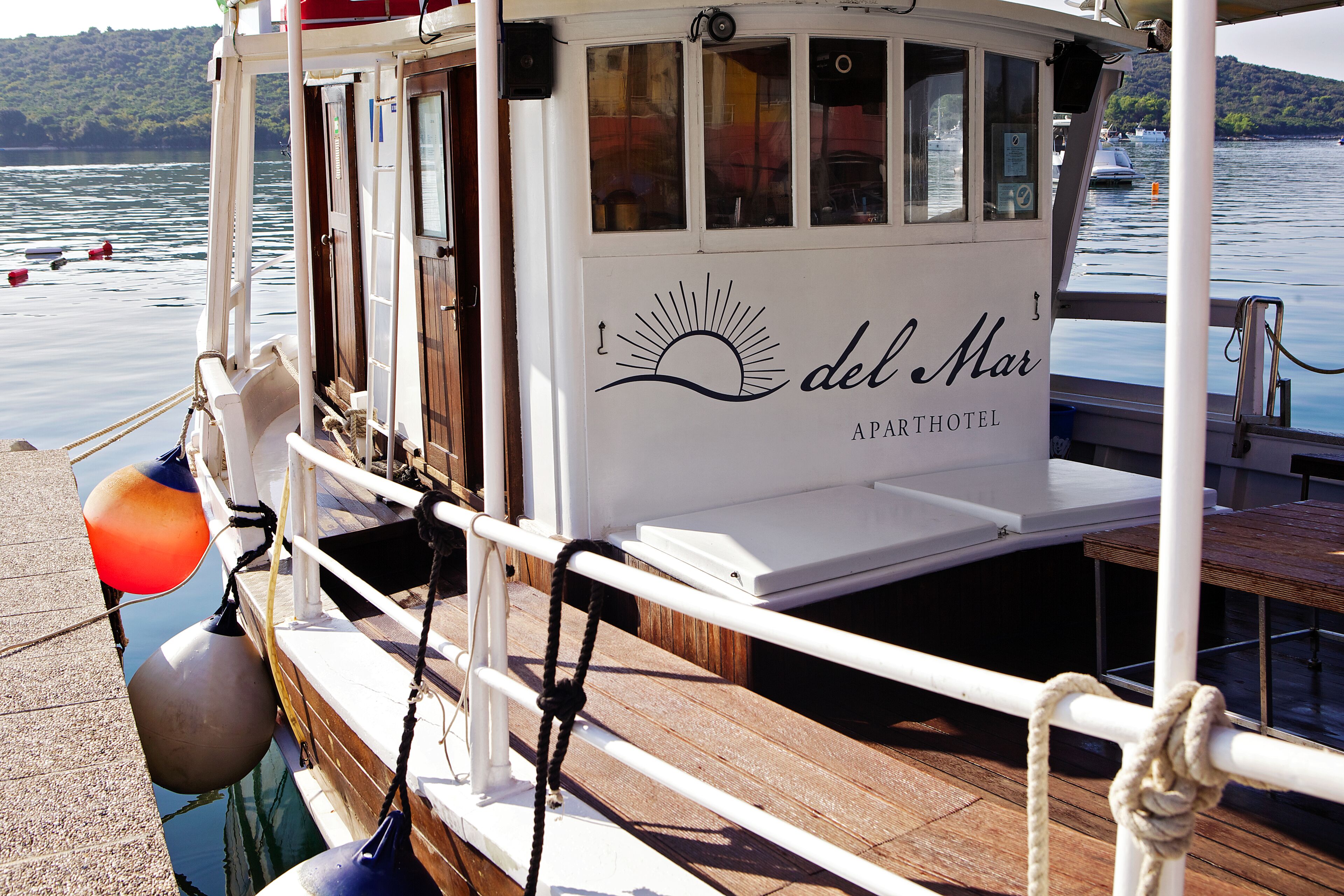 Een boot met een witte buitenkant, een dek en een bord met daarop 'del Mar APARTHOTEL'.