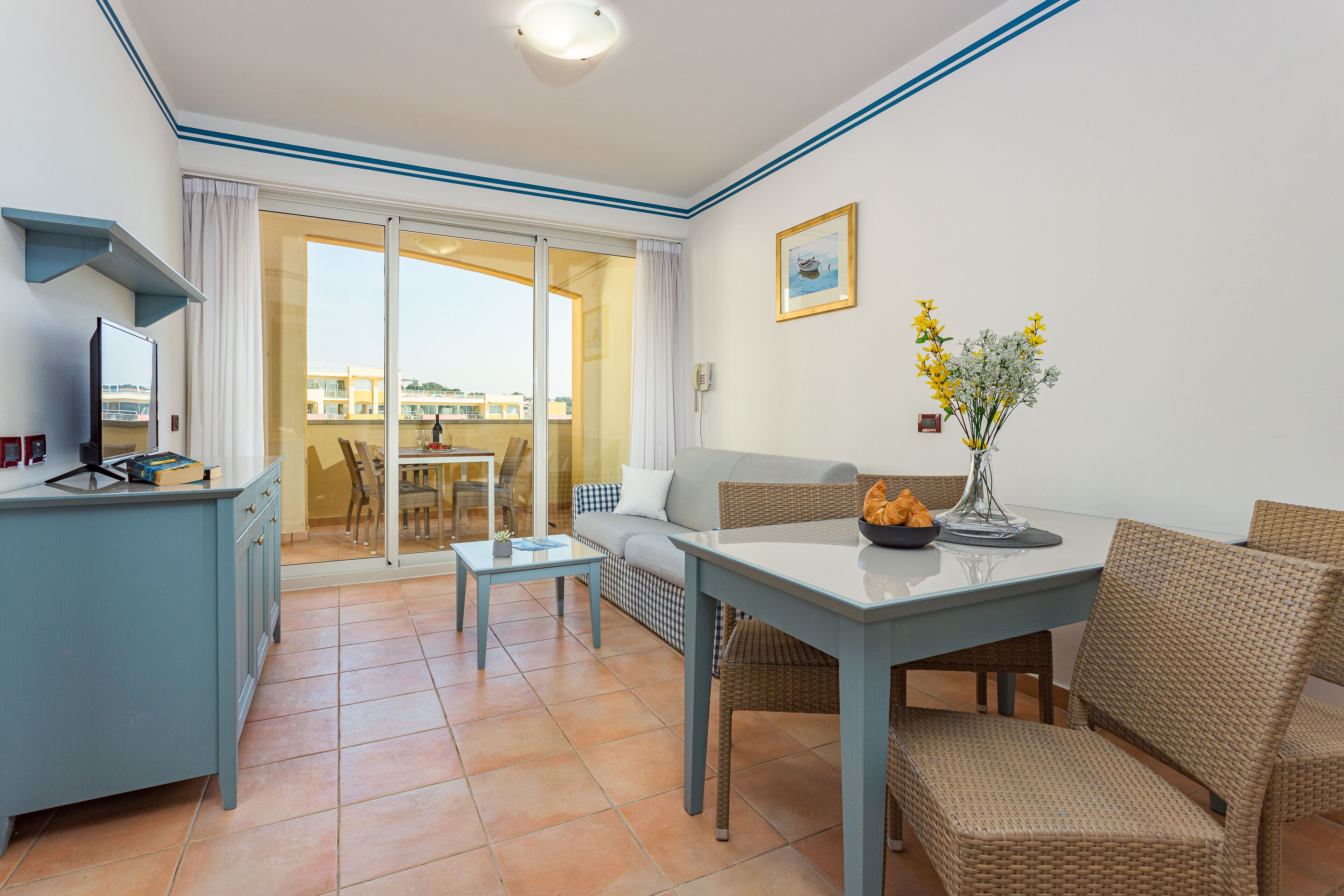 A room with a dining table, chairs, a sofa, a TV, and a view of the outside.