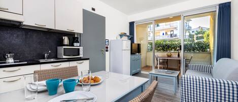 Een moderne keuken met witte kasten, een magnetron en een koffiezetapparaat. Er is een eethoek met een tafel, stoelen en uitzicht op het balkon.