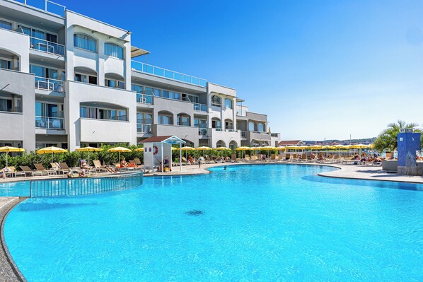 A hotel with a large swimming pool, multiple balconies, and sun loungers.