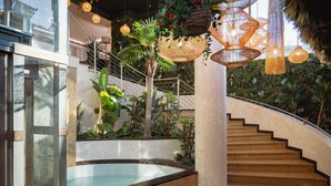 Una escalera interior moderna con barandilla de cristal, rodeada de abundante vegetación e iluminación decorativa.