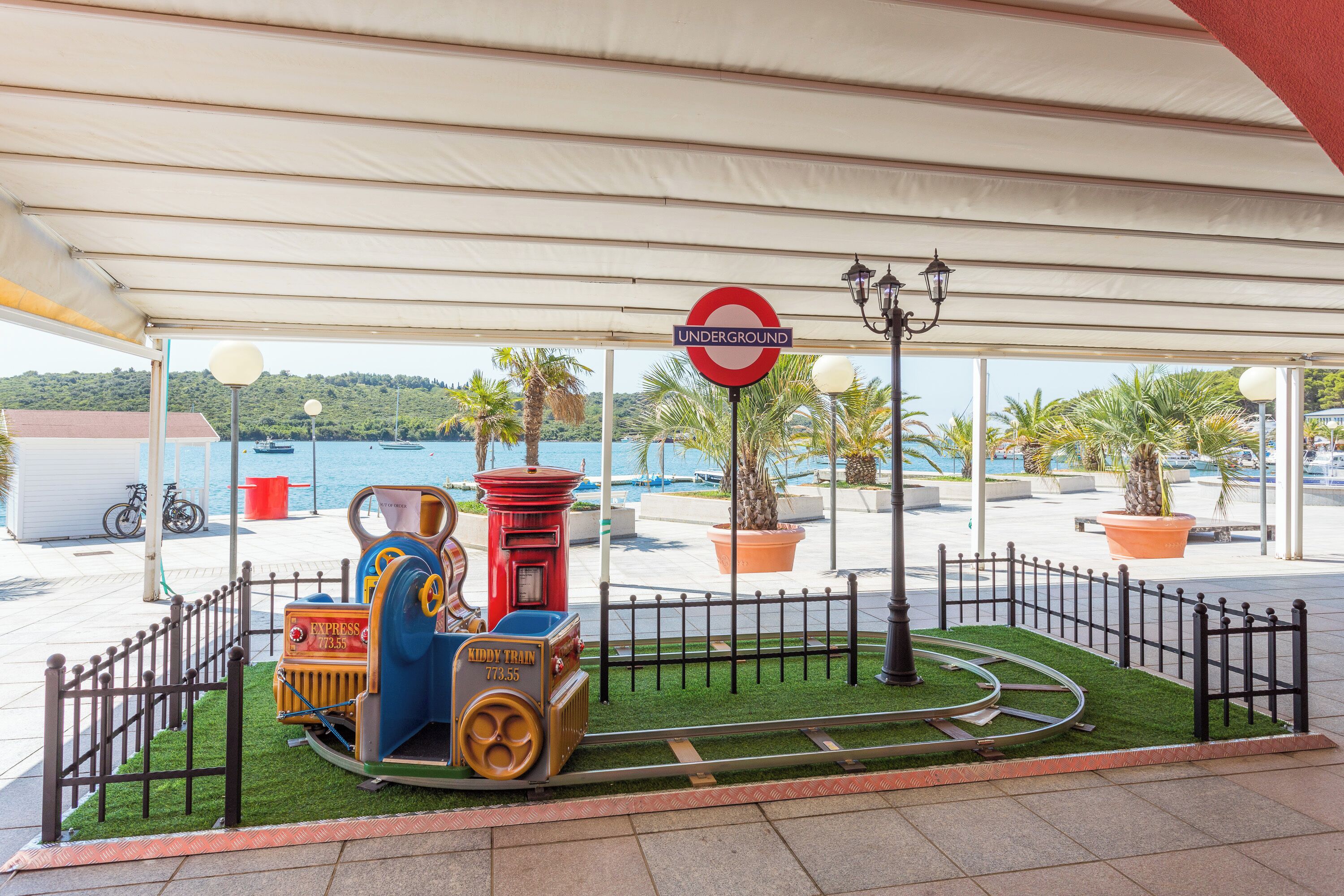 A miniature train set on artificial grass under a canopy, with a 'UNDERGROUND' sign and a lamp post in the background.