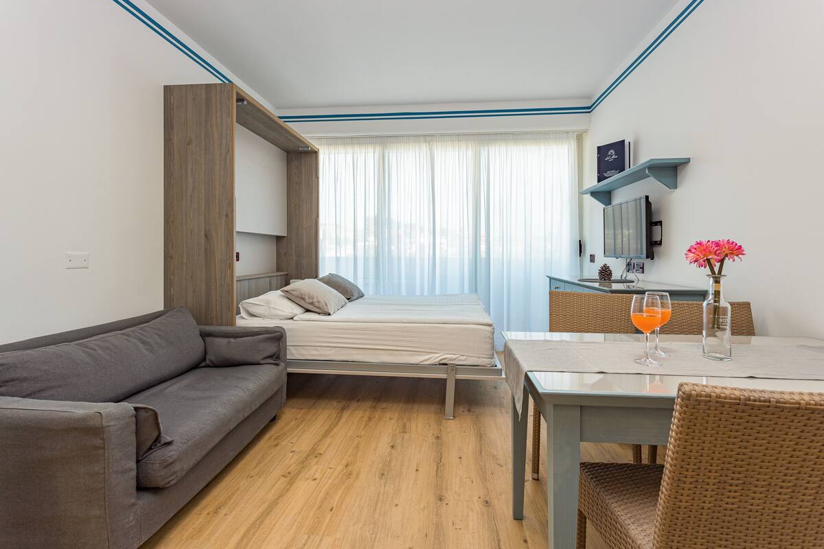 Una habitación de hotel compacta con cama, sofá, mesa de comedor y una pequeña cocina.