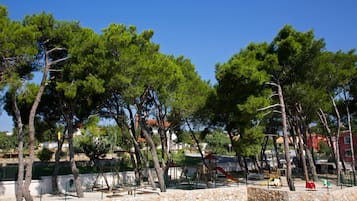 Children can play on the slide and play structures in this shaded outdoor area surrounded by trees.