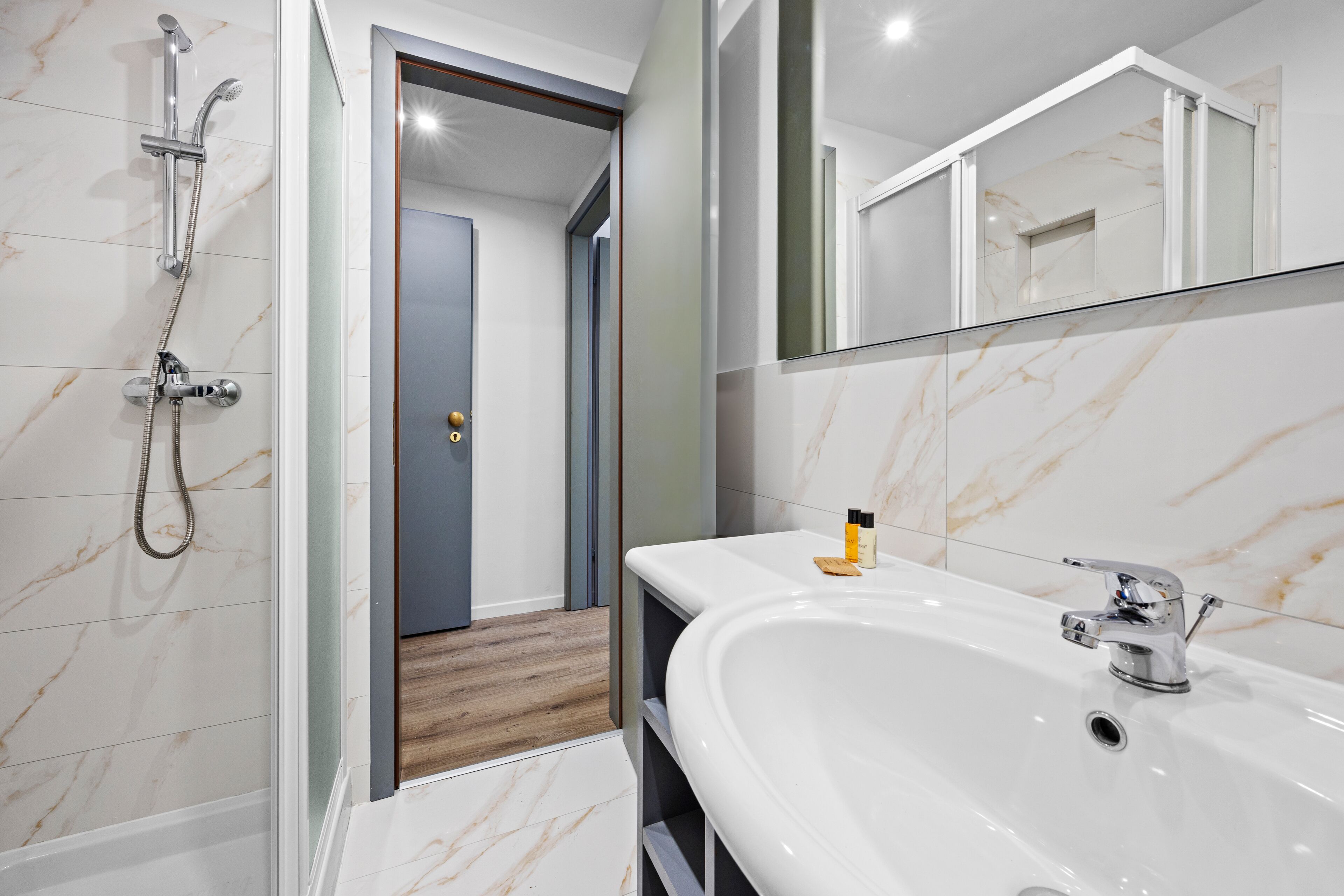 Un bany modern amb un mirall gran, un lavabo blanc i una zona de dutxa.