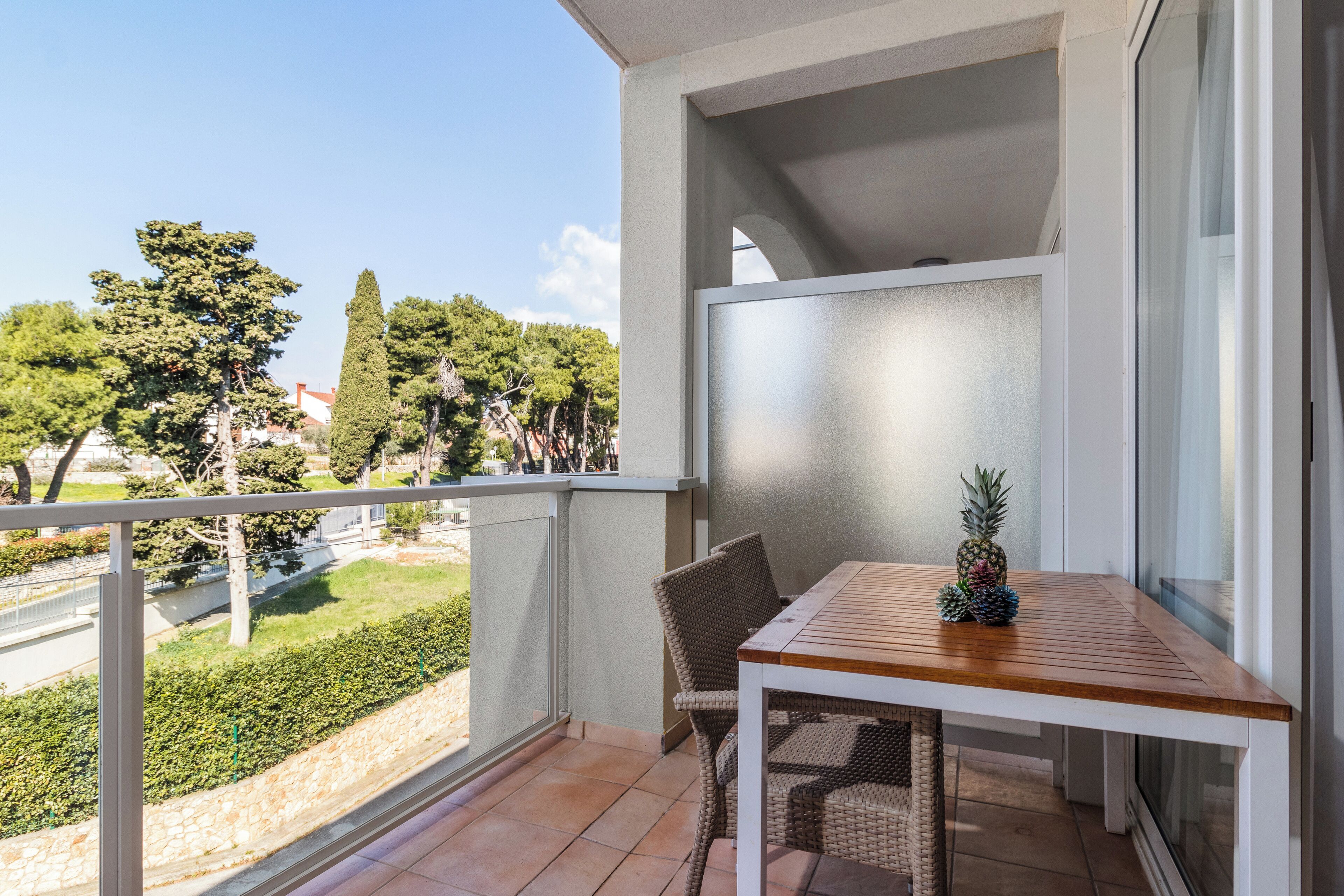 A balcony with a table and chairs, overlooking a green landscape and trees.