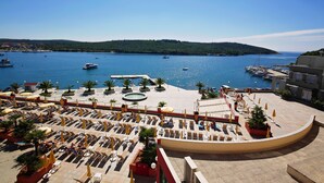 Un hotel frente al mar con zonas de estar al aire libre, piscina y barcos al fondo.