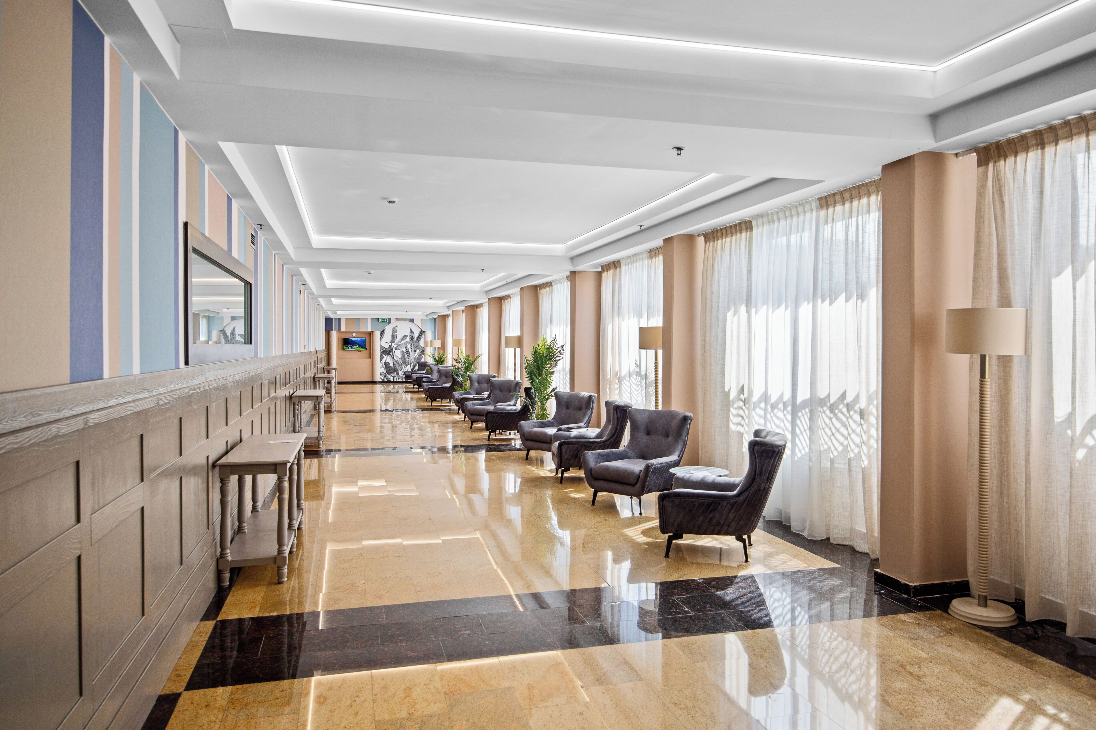 A hotel lobby with a long reception desk, multiple armchairs, and a polished marble floor.