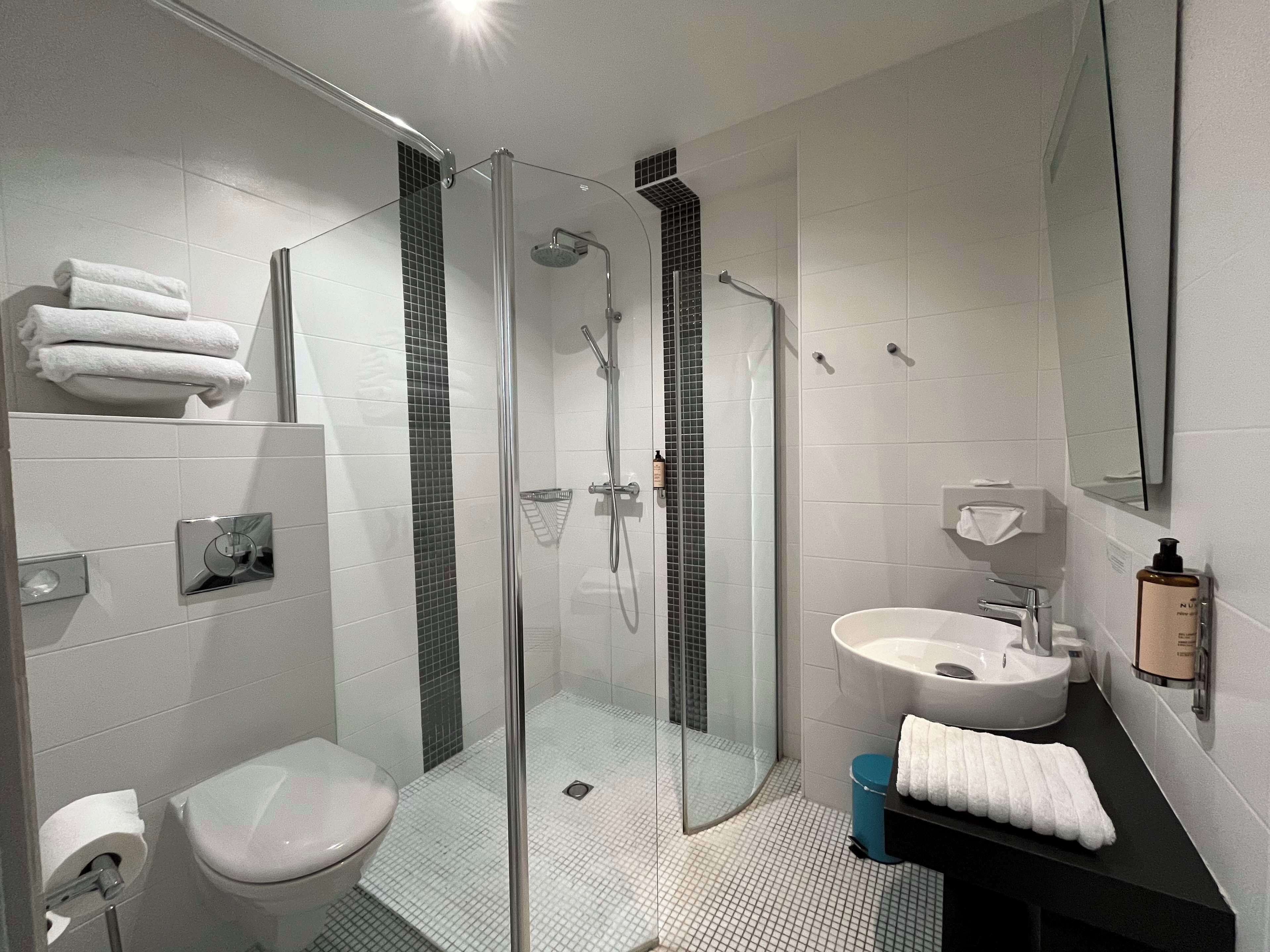 A modern bathroom with a glass-enclosed shower, a white toilet, and a sink with a mirror.