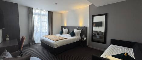 A modern hotel room with a large bed, a desk, a chair, and a TV.