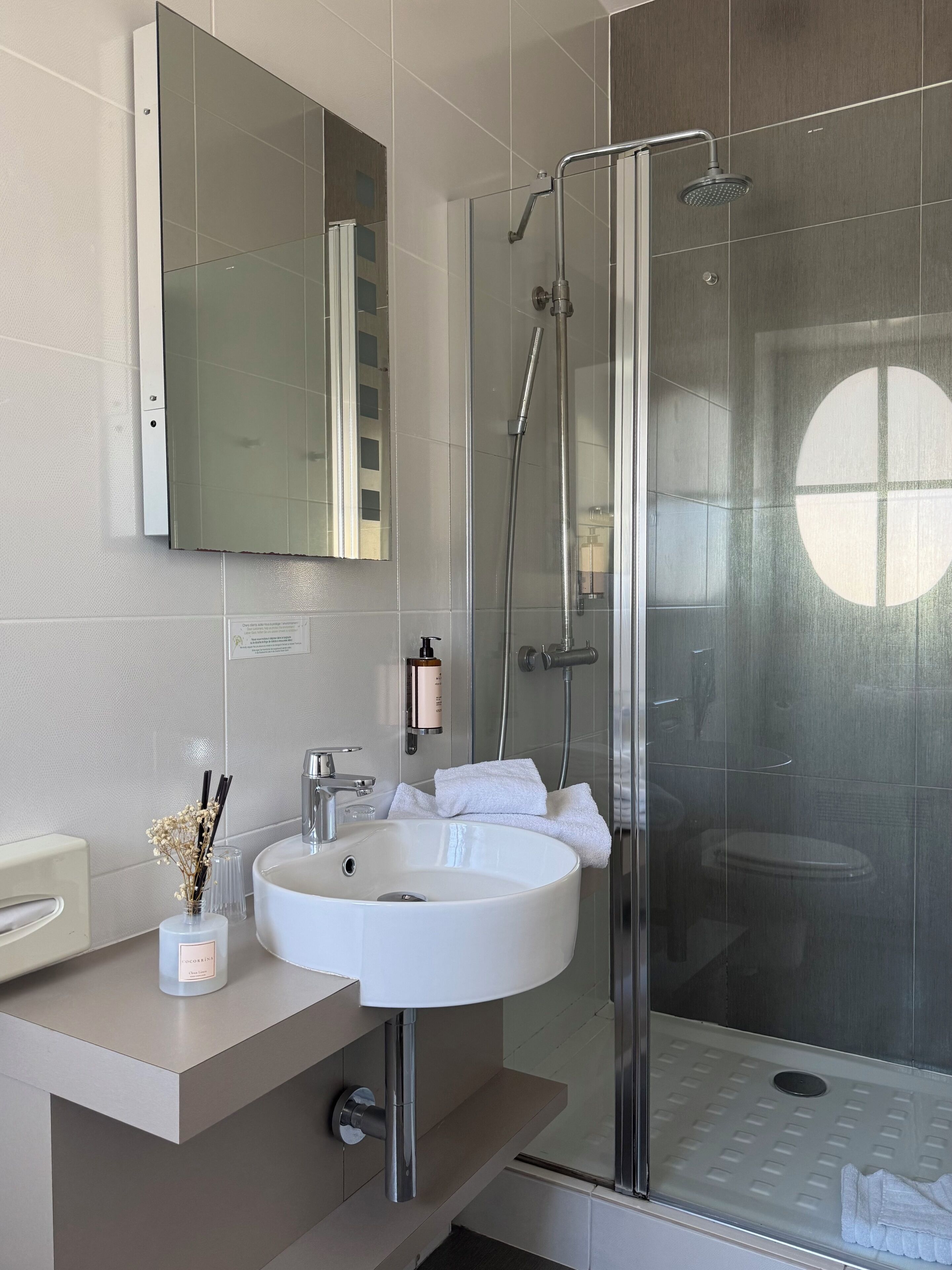 Een moderne badkamer met een douchecabine van glas, een witte wastafel en een spiegel erboven.