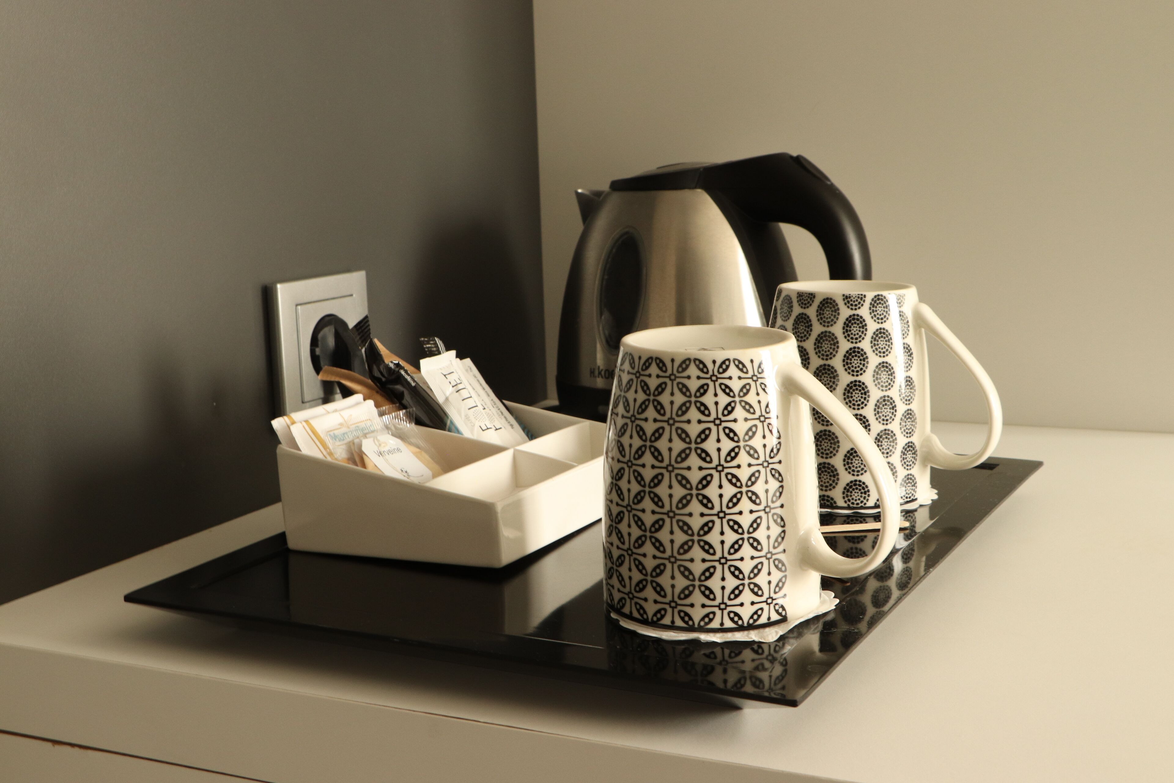 Una bandeja con dos tazas decoradas, una tetera y una caja con un tenedor, cuchara y servilletas.