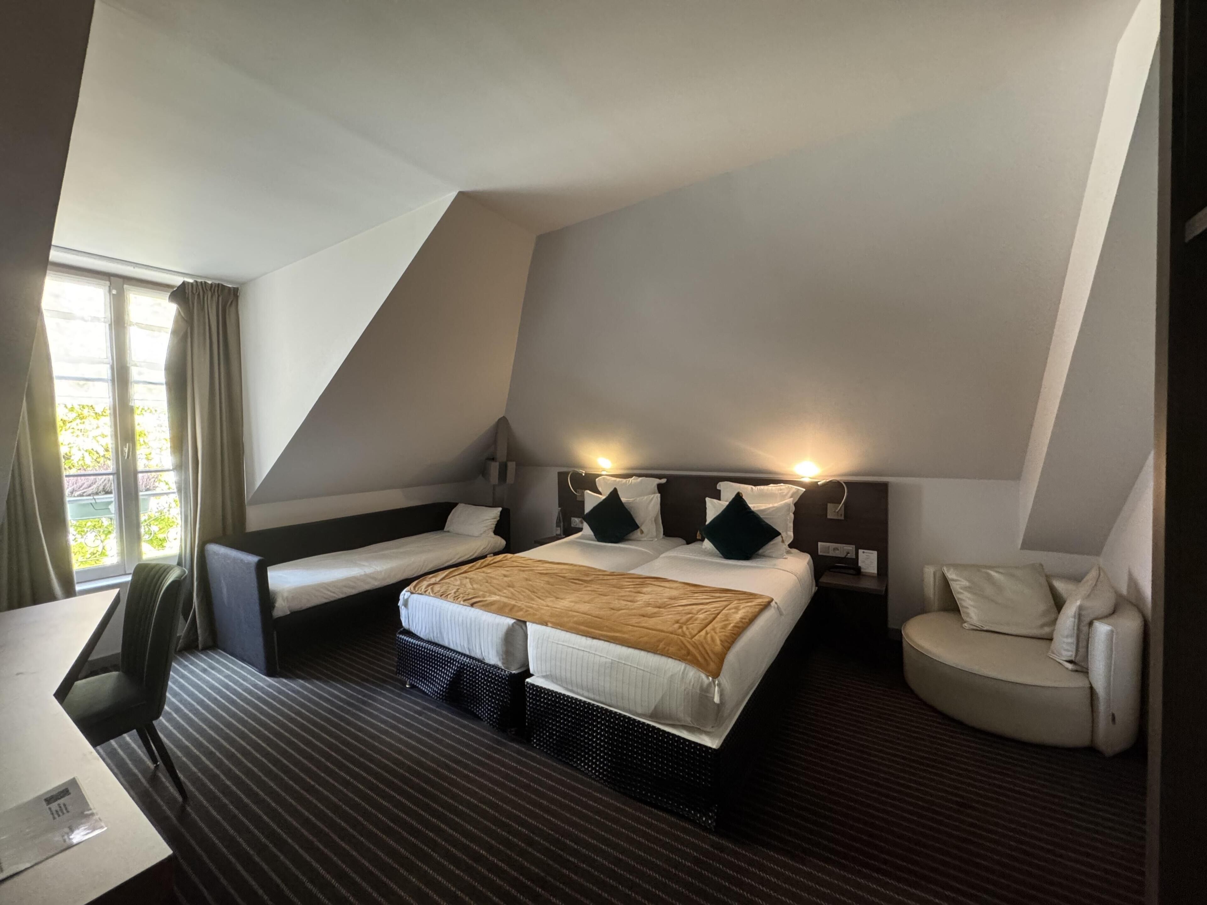 Une chambre d’hôtel avec un grand lit, deux petits lits, un bureau et une chaise.