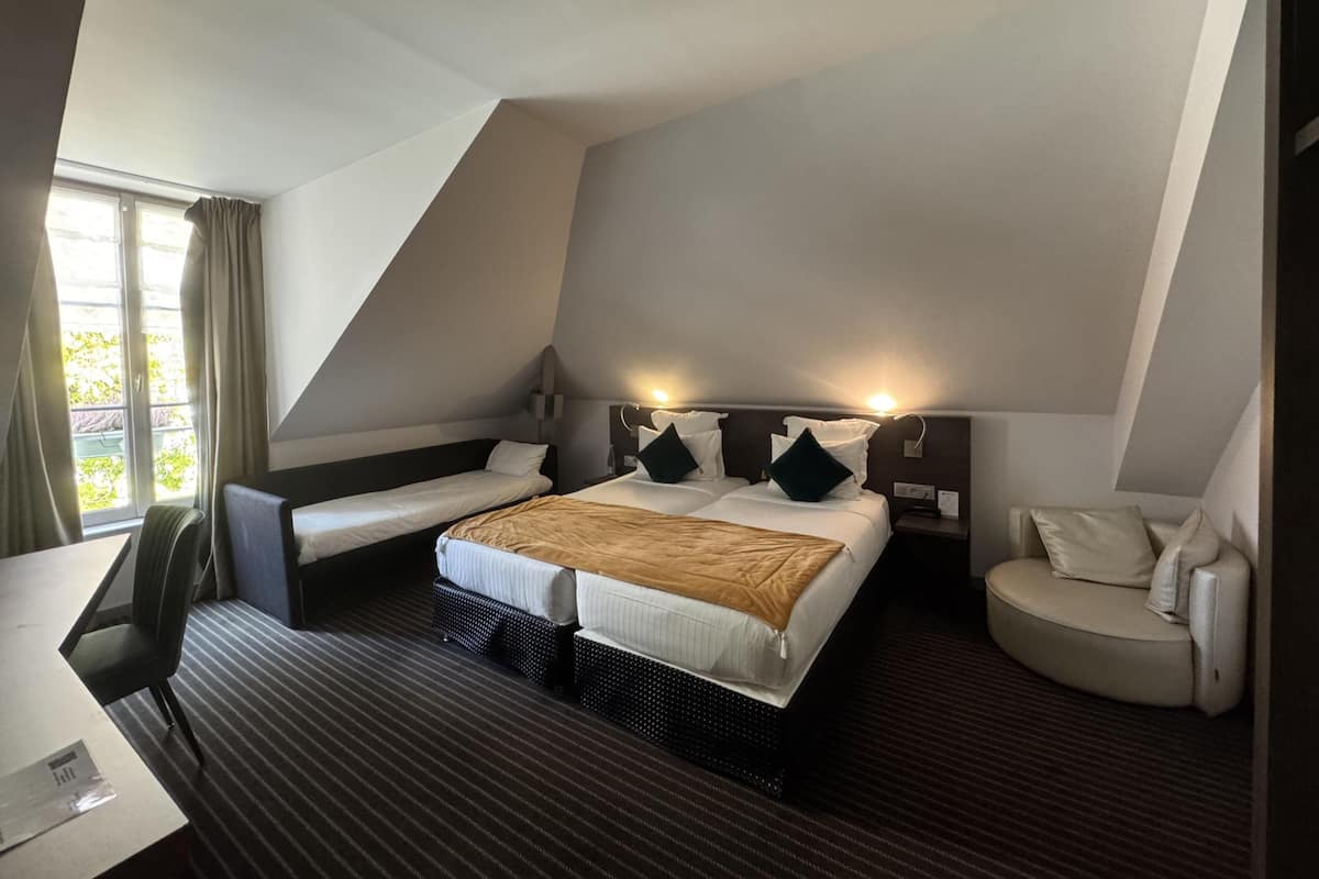 Une chambre d’hôtel avec un grand lit, deux petits lits, un bureau et une chaise.