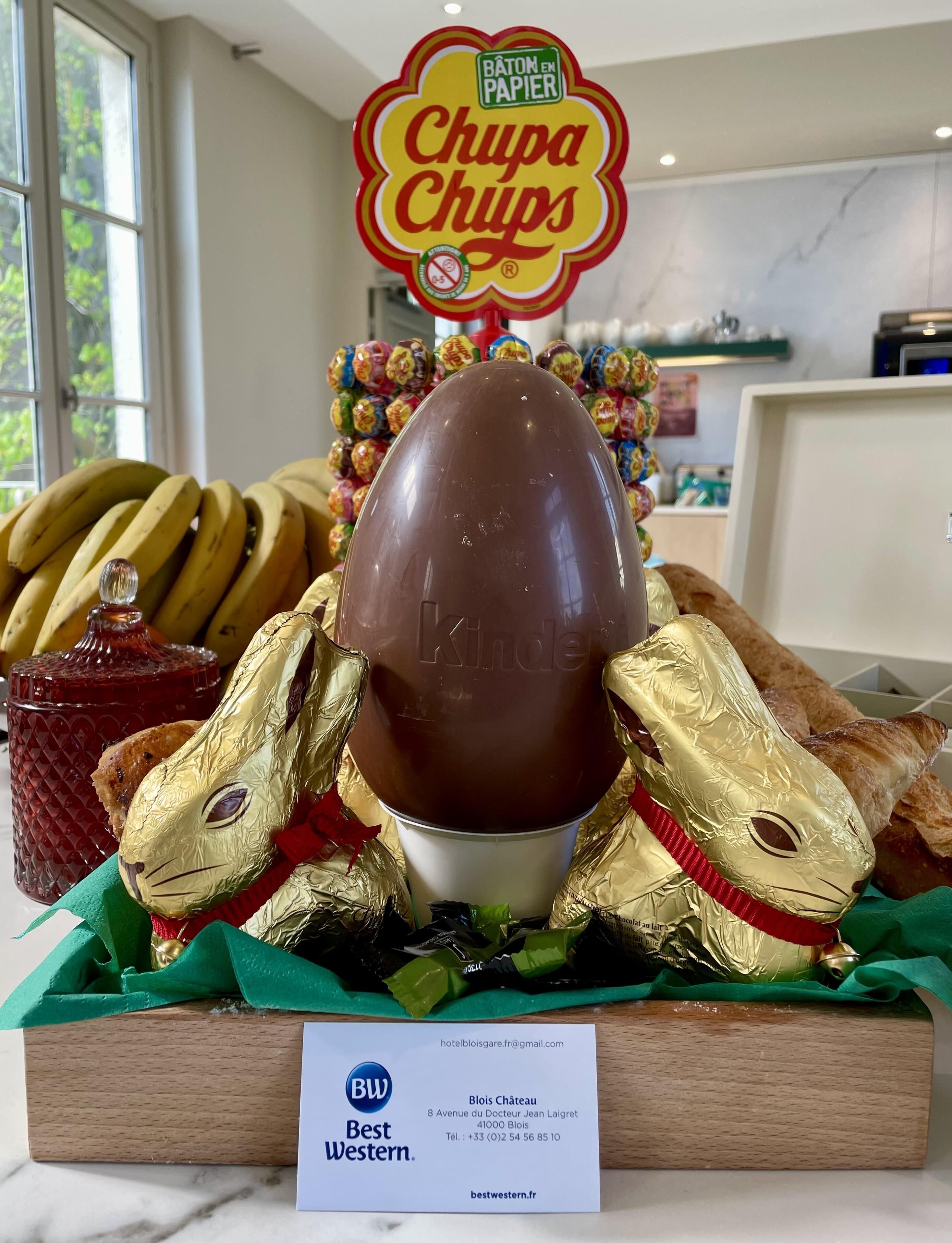 Un huevo de chocolate rodeado de dulces cubiertos de chocolate, un cartel que dice 'Chupa Chups' y un cartel de Best Western.