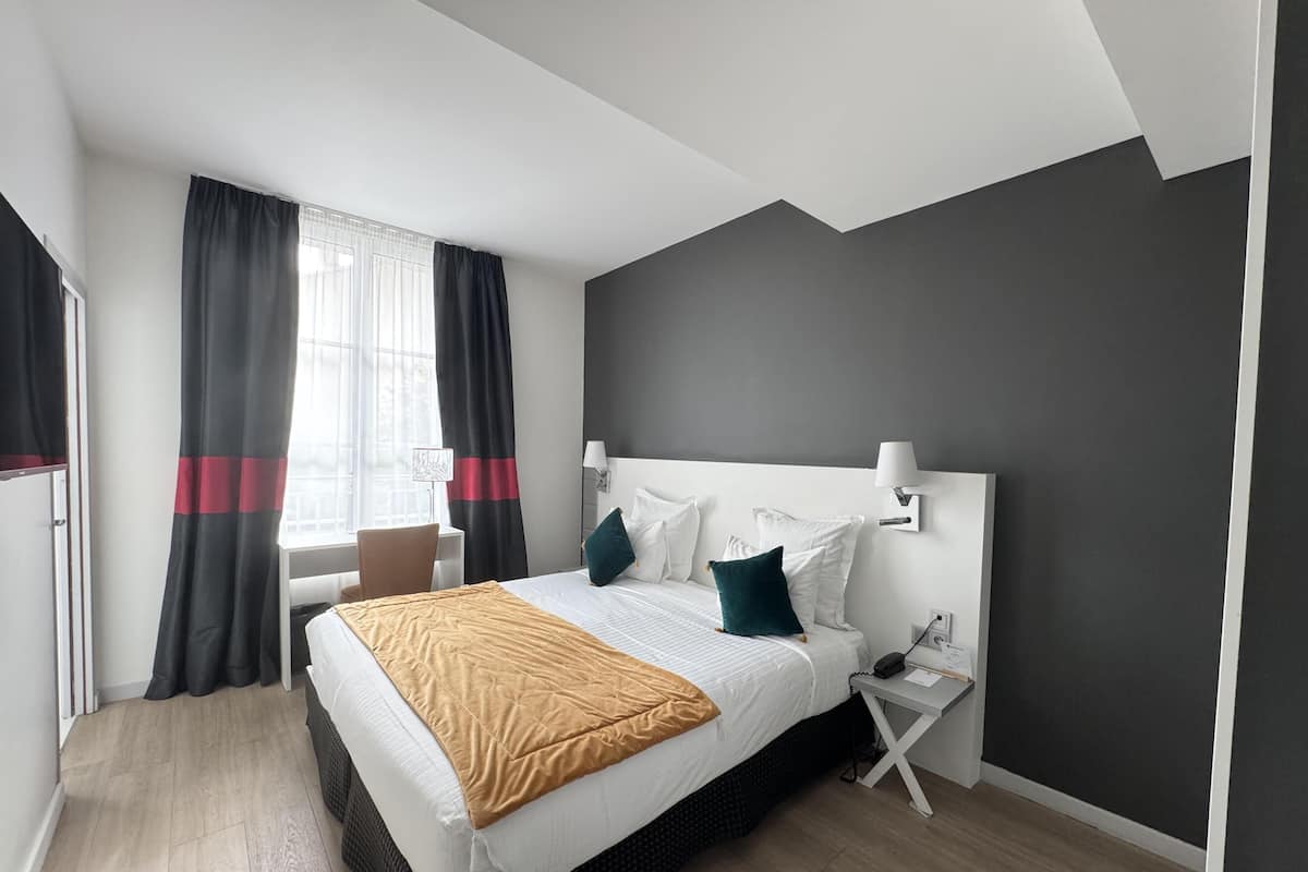 Une chambre d’hôtel moderne avec un grand lit, une table de chevet, une chaise et une fenêtre avec des rideaux.