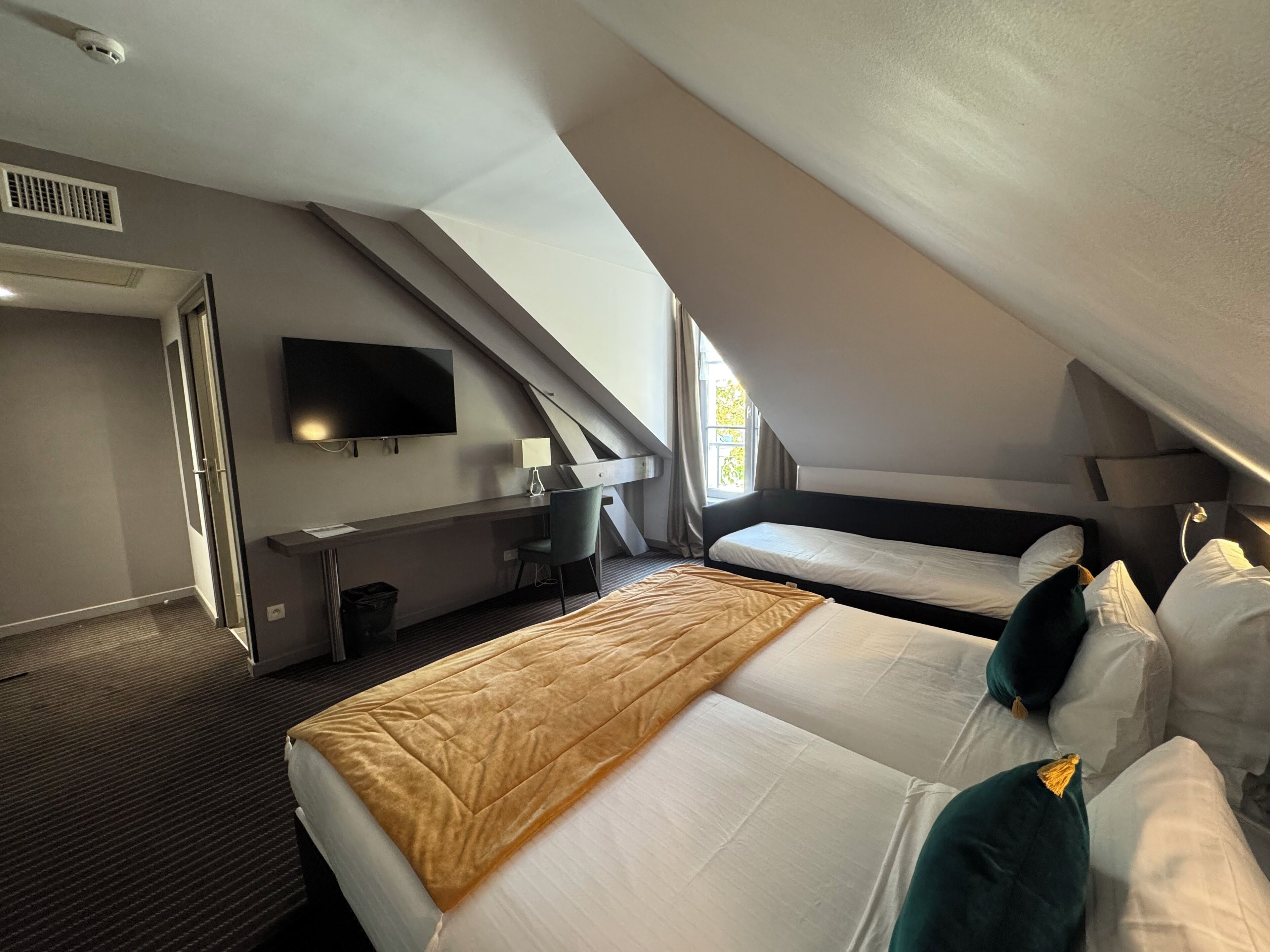 Une chambre d’hôtel avec un grand lit, un bureau avec une chaise, un téléviseur à écran plat et une fenêtre avec des rideaux.