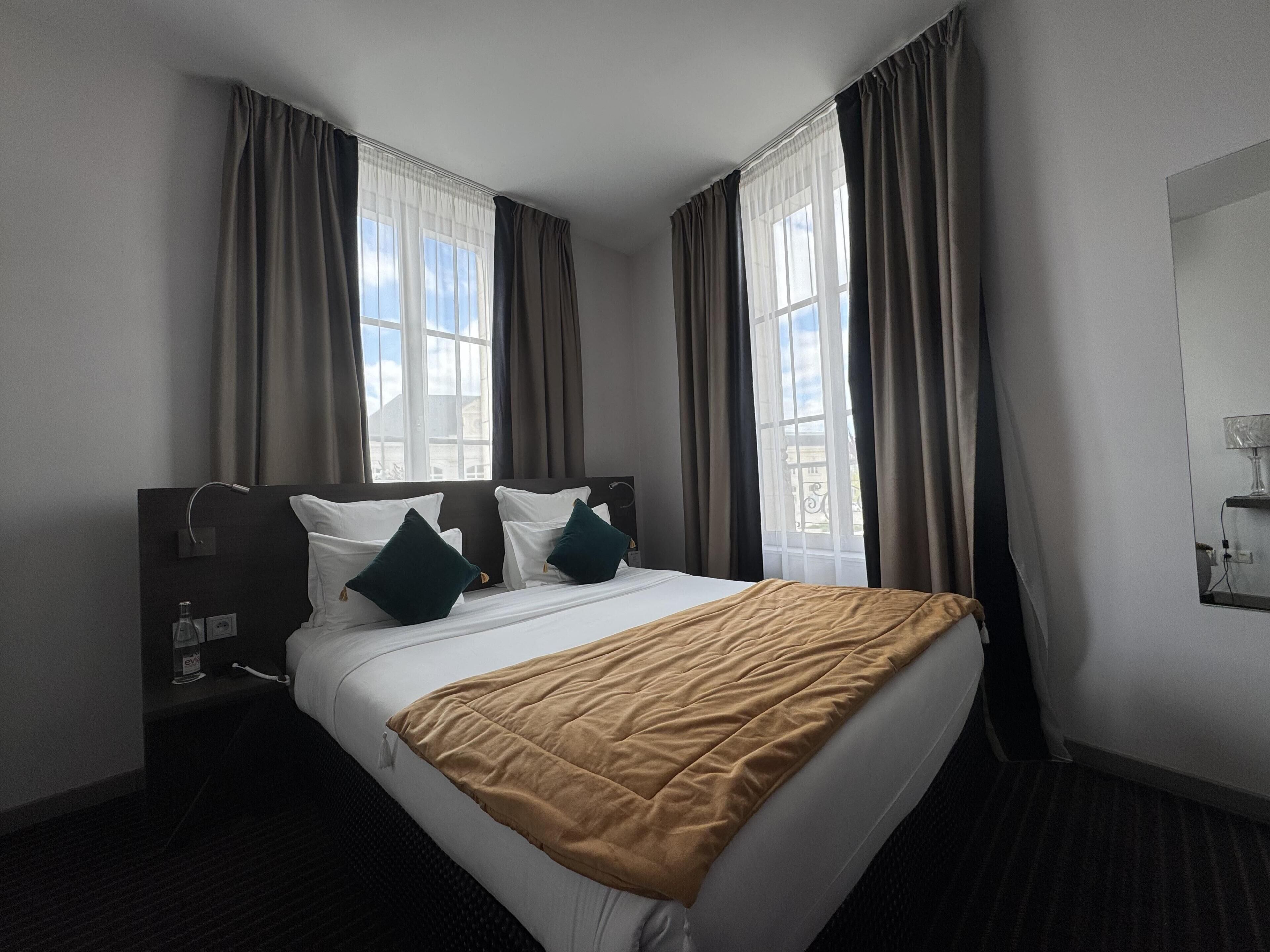 Une chambre d’hôtel avec un lit, des rideaux, une table de chevet et une fenêtre donnant sur un paysage agréable.