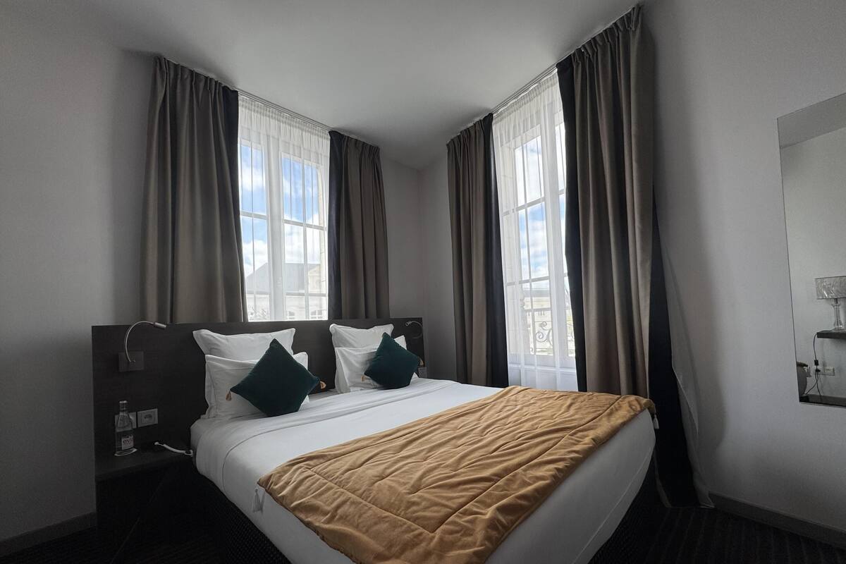 Une chambre d’hôtel avec un lit, des rideaux, une table de chevet et une fenêtre donnant sur un paysage agréable.