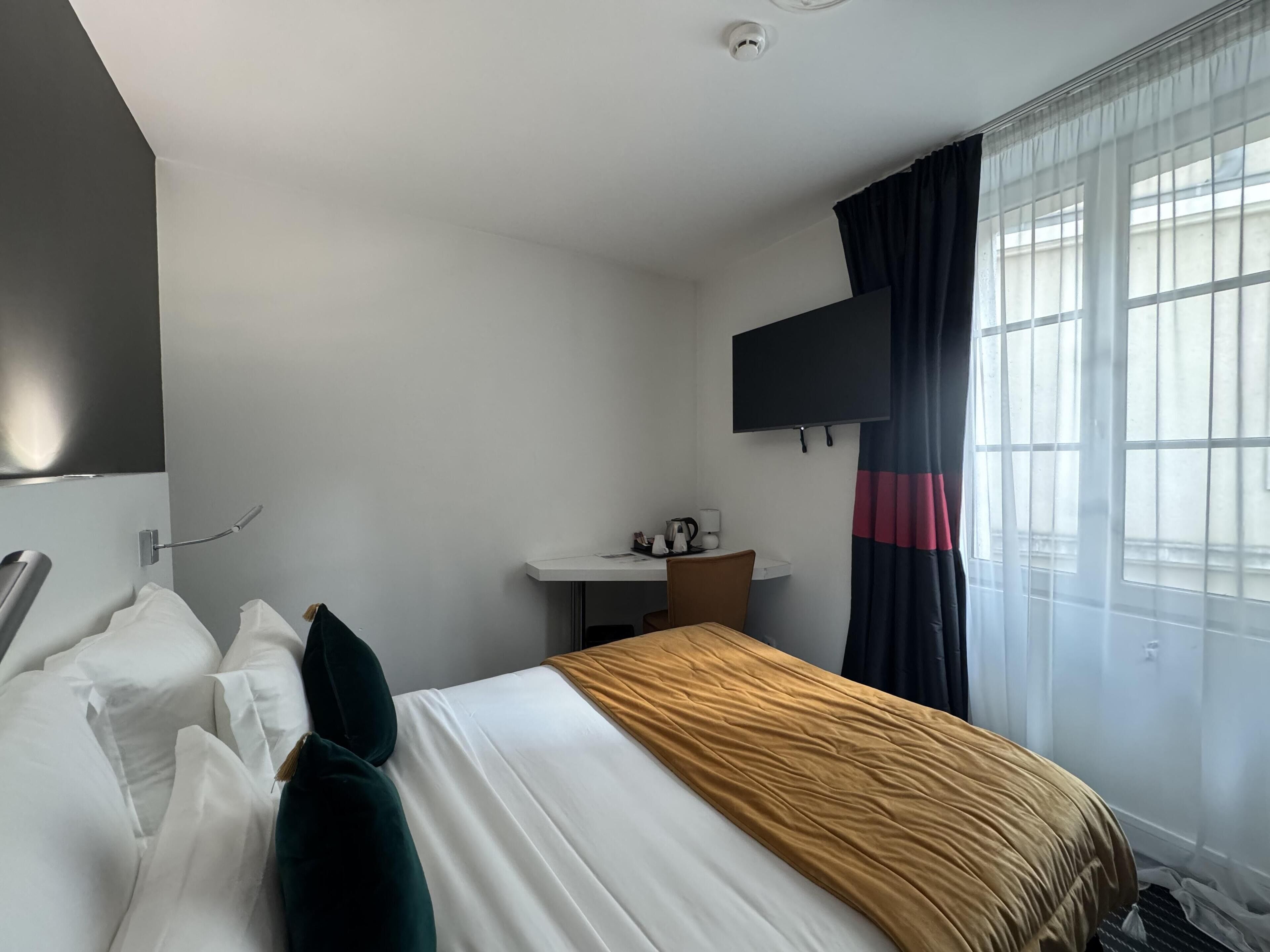 Ein Hotelzimmer mit einem Bett, einem Schreibtisch, einem Sessel, einem Flachbildfernseher und einem Vorhangfenster.