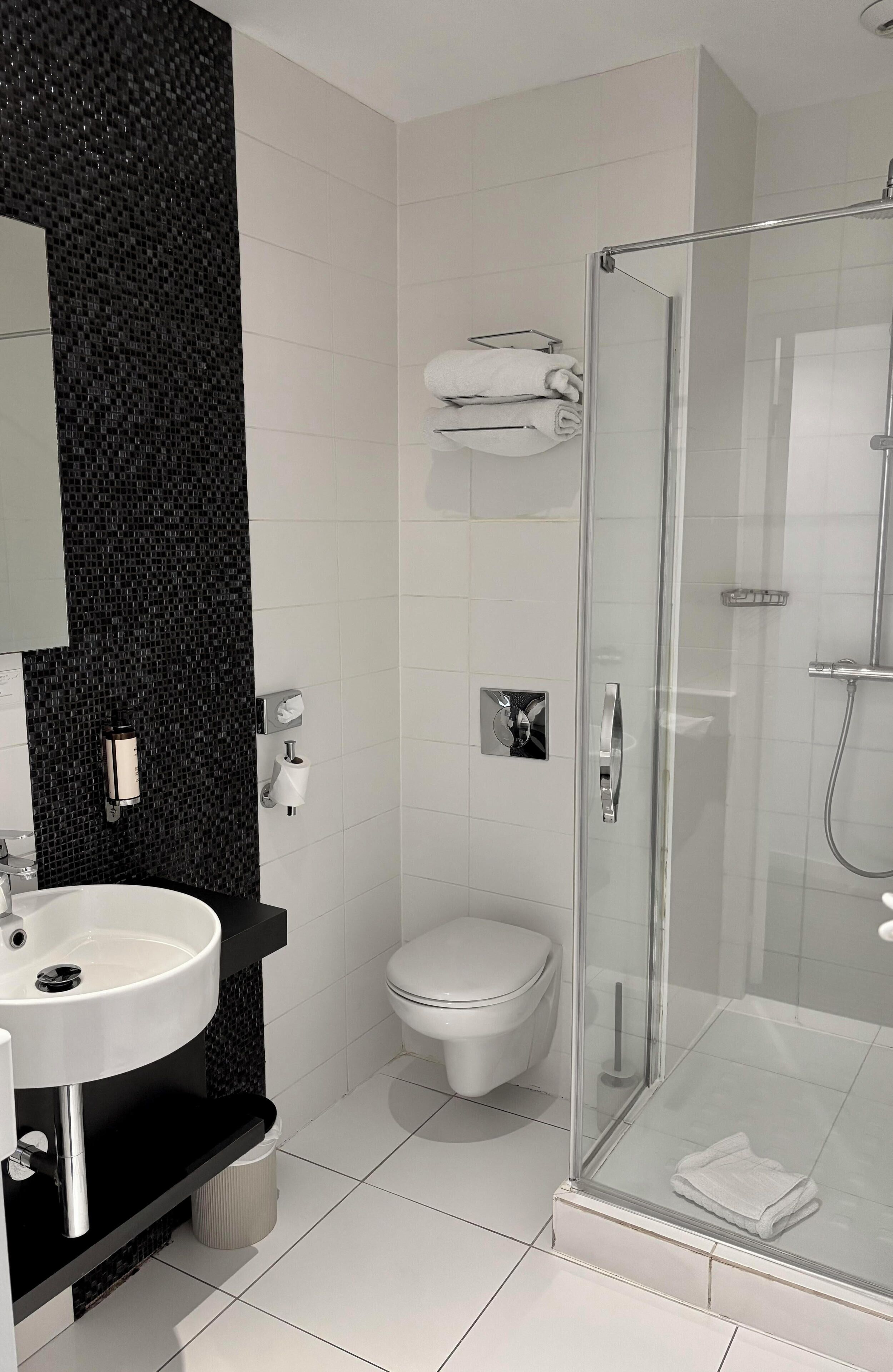 A modern bathroom with a black mosaic backsplash, a white sink, a toilet, and a glass-enclosed shower area.