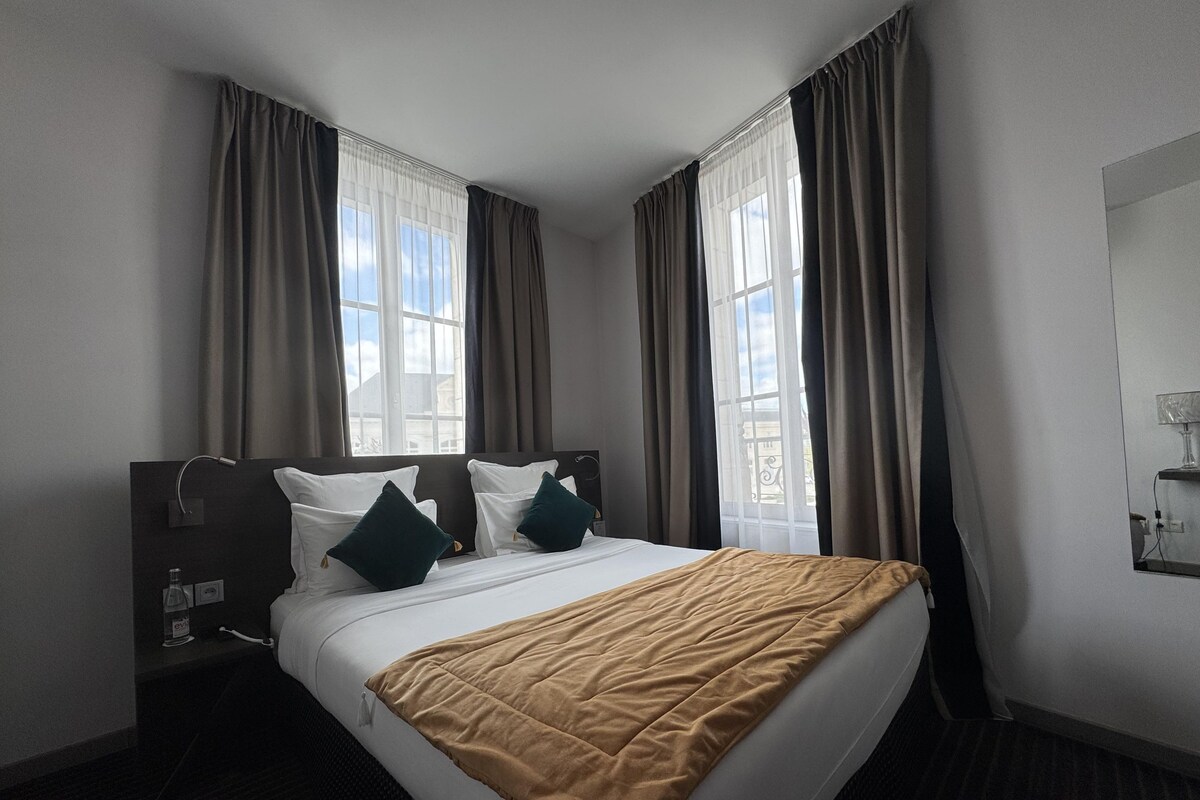 Een hotelkamer met een bed, gordijnen, een nachtkastje en een raam met uitzicht.