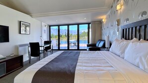 Habitación de hotel con una cama grande, un escritorio, una silla y vistas a las montañas a través de las ventanas.
