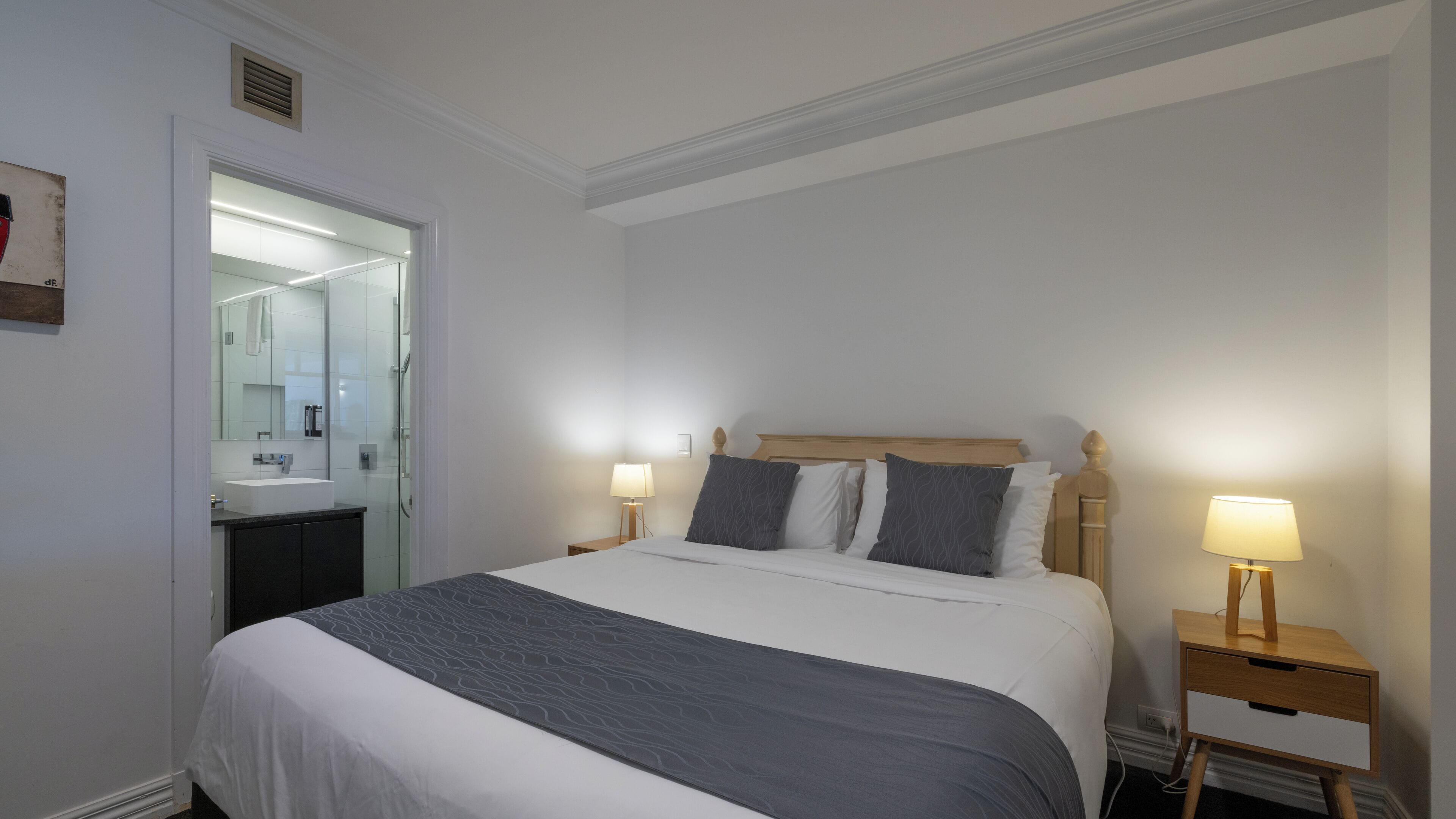 Een hotelkamer met een groot bed, bedlampen, een nachtkastje en een badkamer zichtbaar door een geopende deur.