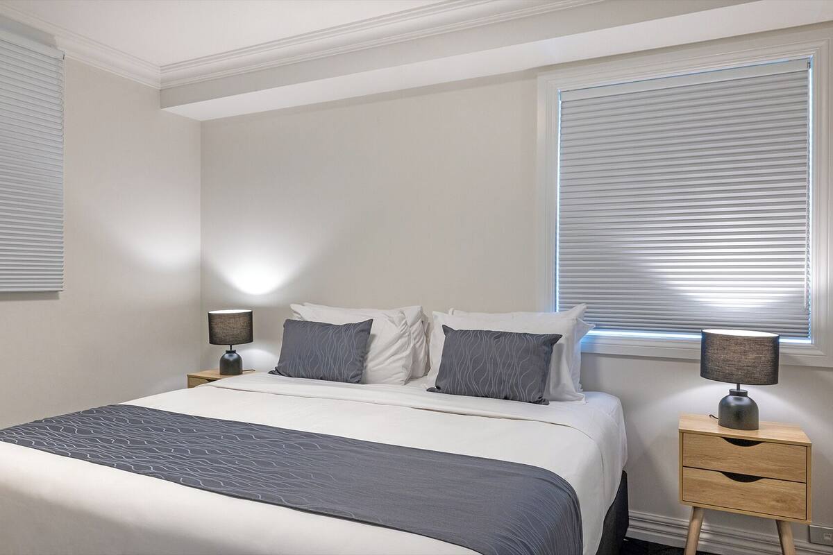 Un dormitorio con una cama, dos mesitas de noche y dos lámparas.