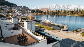 Un hotel con terraza en la azotea, muelle y vistas a un lago con montañas al fondo.