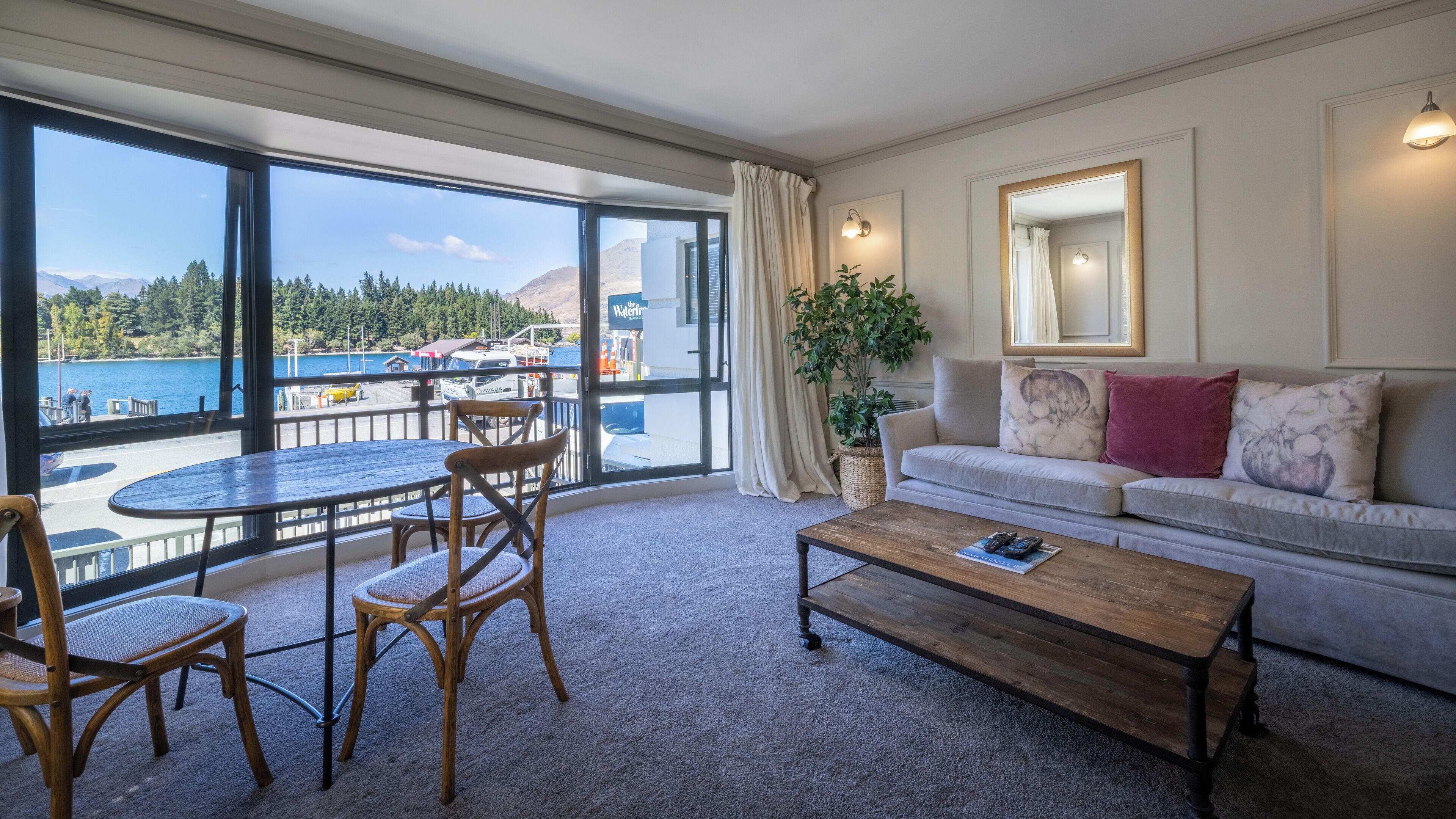 Ein geräumiger Wohnbereich mit Balkon und Blick auf ein Gewässer, inklusive Sofa, Couchtisch und Esstisch mit Stühlen.