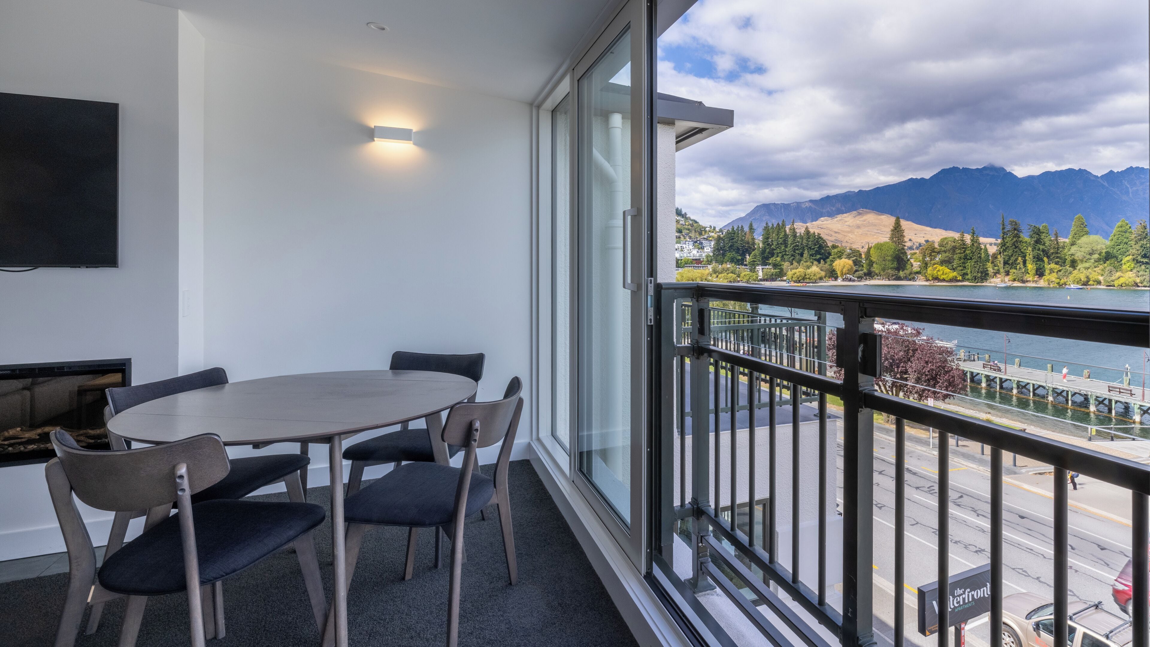 A balcony with a table and chairs, overlooking a lake and mountains.