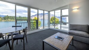 Una habitación moderna con amplios ventanales que ofrecen vistas a un lago y montañas. Hay una mesa con sillas, un sofá y una mesita de centro.