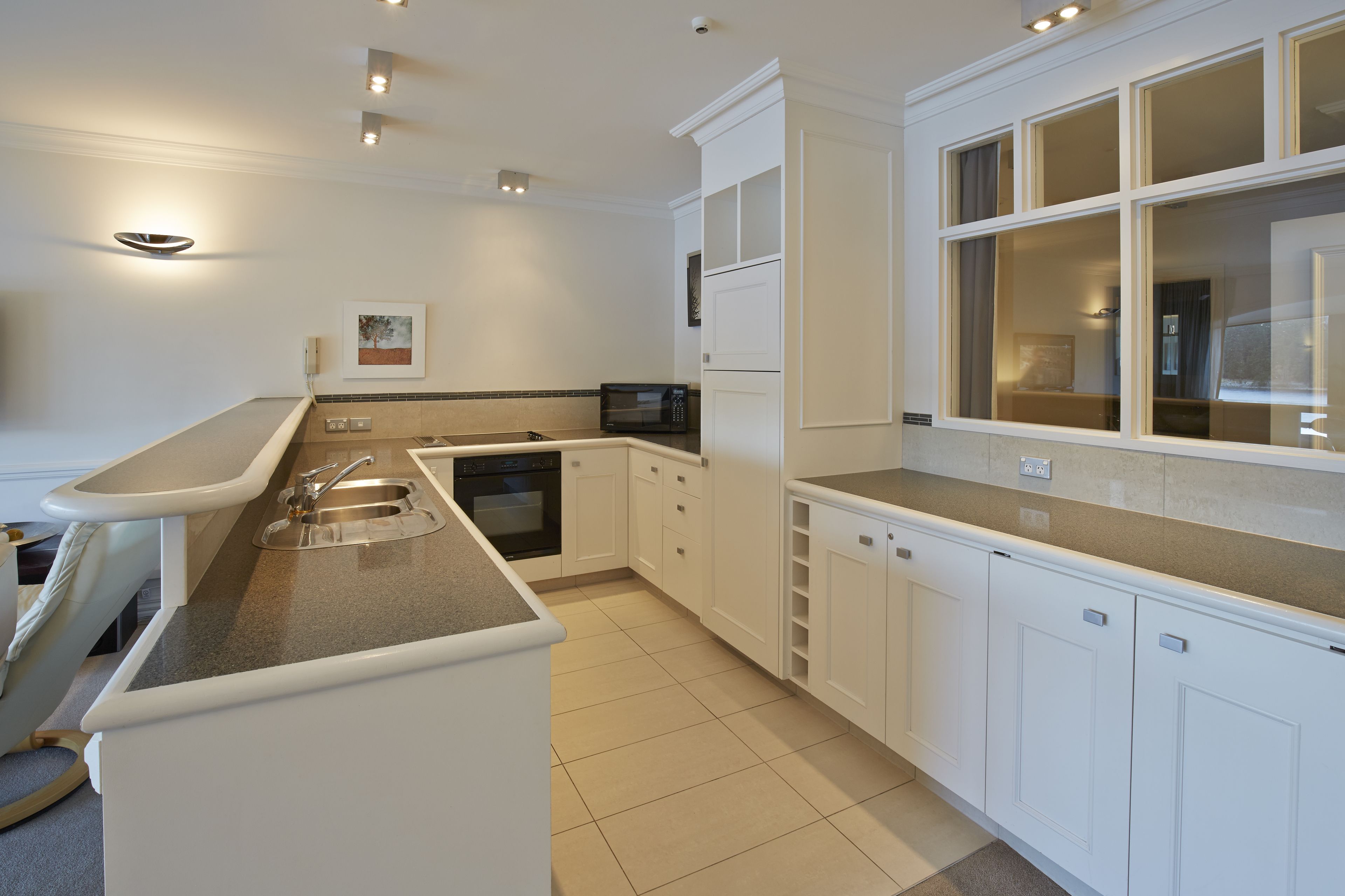 A modern kitchen with white cabinetry, a built-in microwave, and a large window.