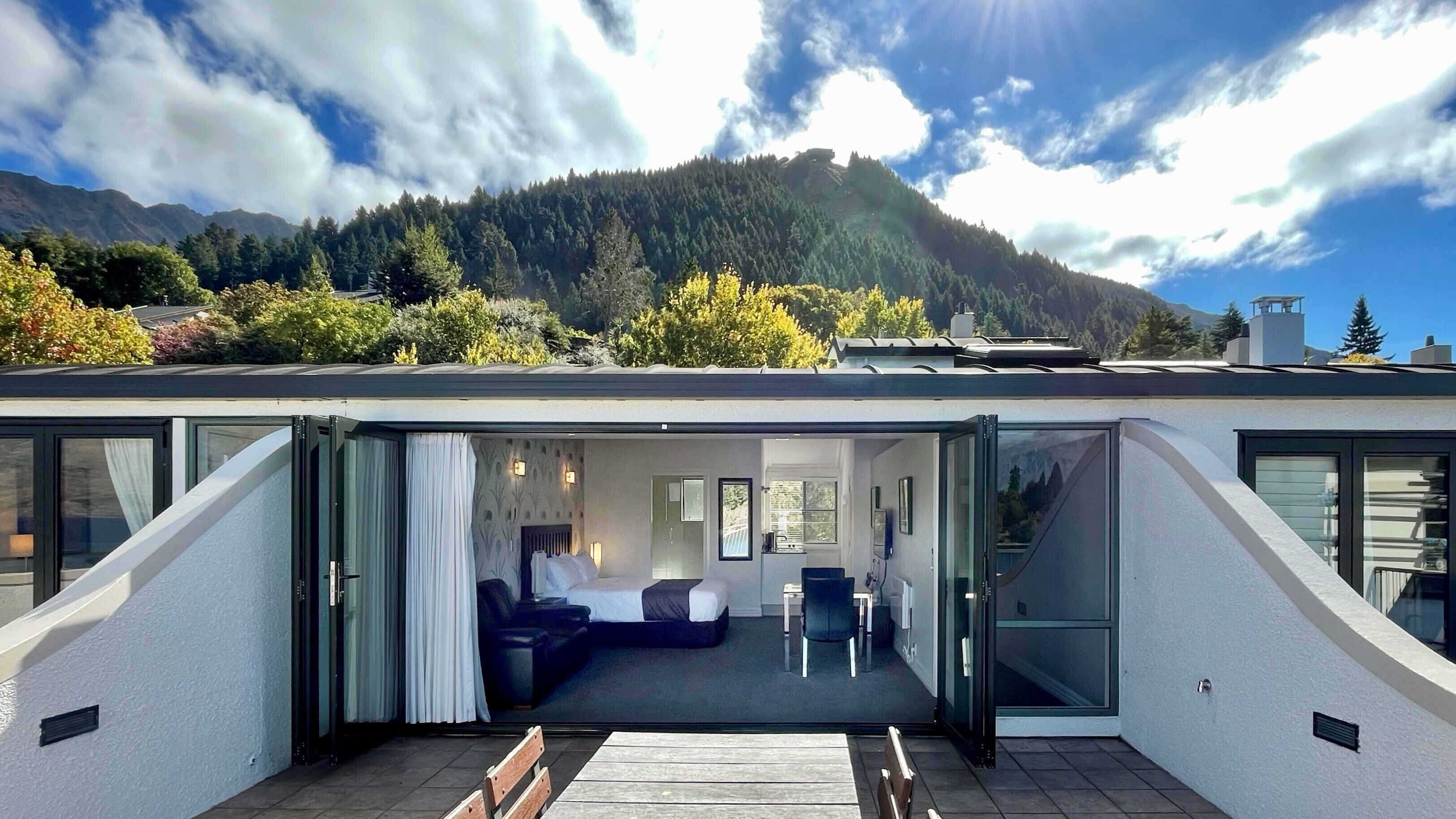 A modern hotel room with a bed, seating area, and large windows offering mountain views.