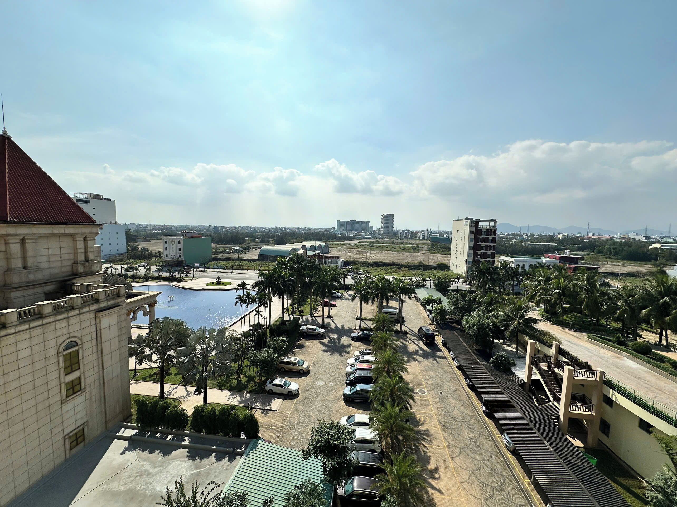 A parking area with multiple cars, palm trees, and a building with a red roof.