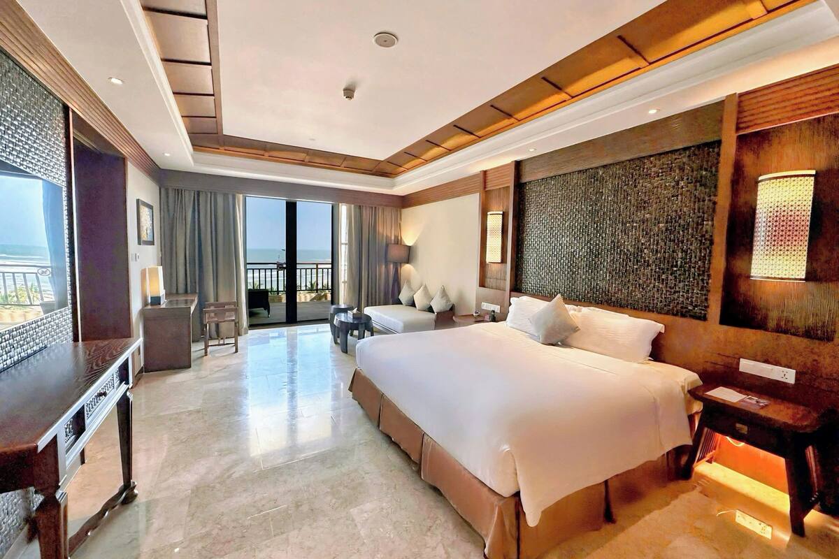 Ein Hotelzimmer mit einem großen Bett, einem Schreibtisch und einem Balkon mit Blick.