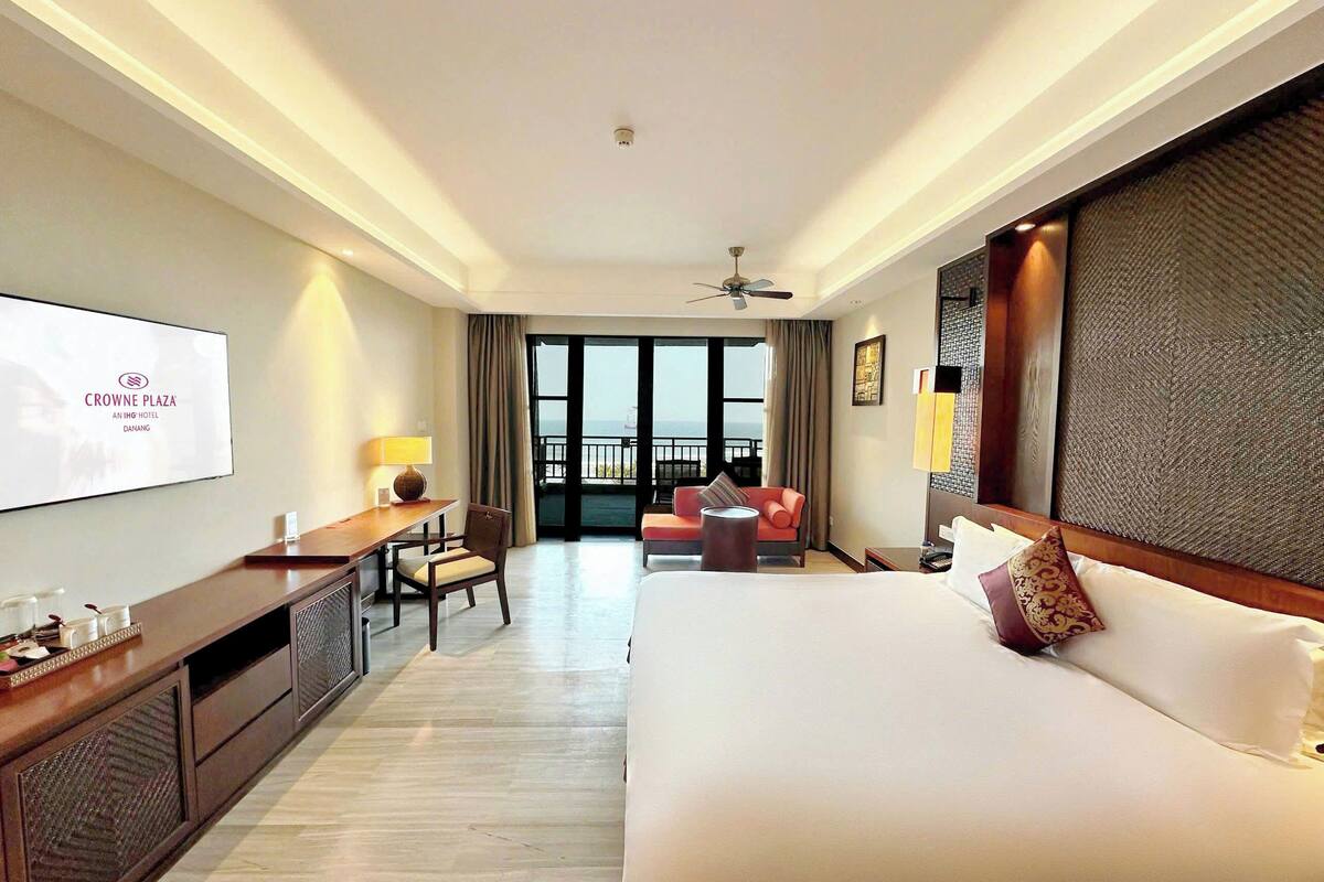 Ein Hotelzimmer mit Bett, Schreibtisch, Stuhl, Fernseher und einem Balkon mit Blick.