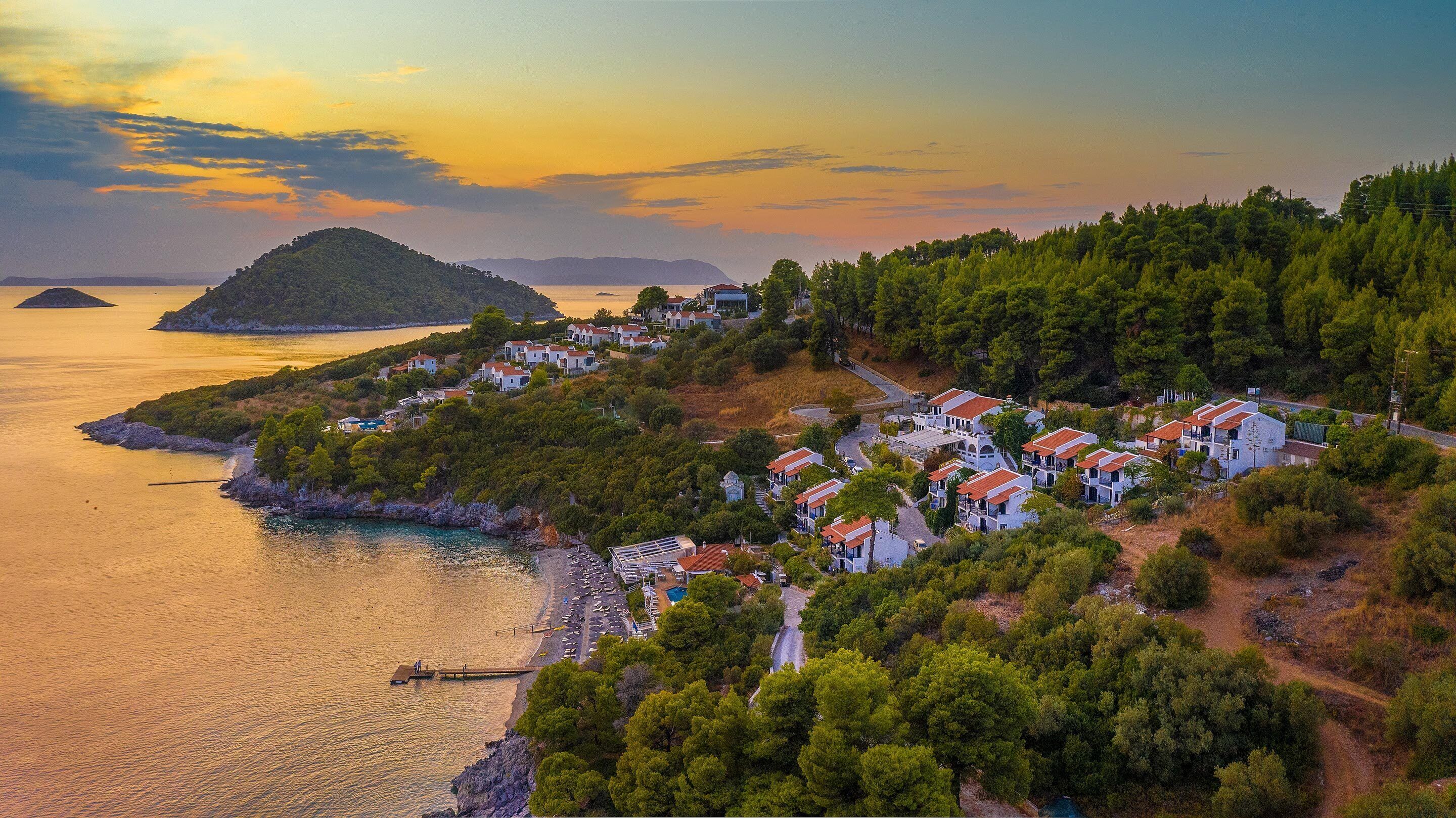 Un borgo costiero con case bianche, una spiaggia e una piccola isola sullo sfondo.