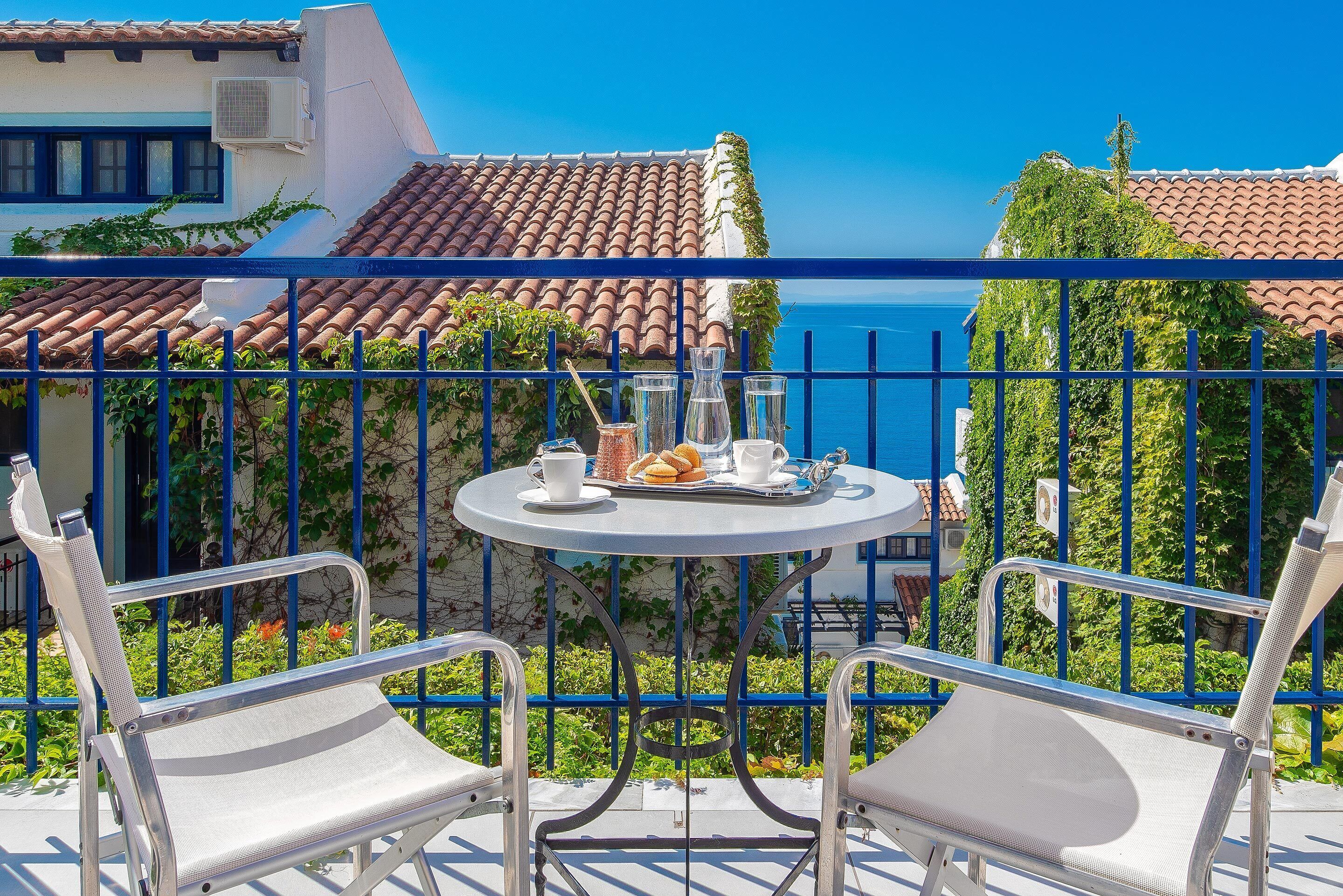 A balcony with a table set for two, a chair, and a view of the sea.