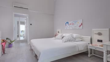Un dormitorio con una cama blanca, una mesita de noche, un aparador, una planta en maceta y un cuadro en la pared.