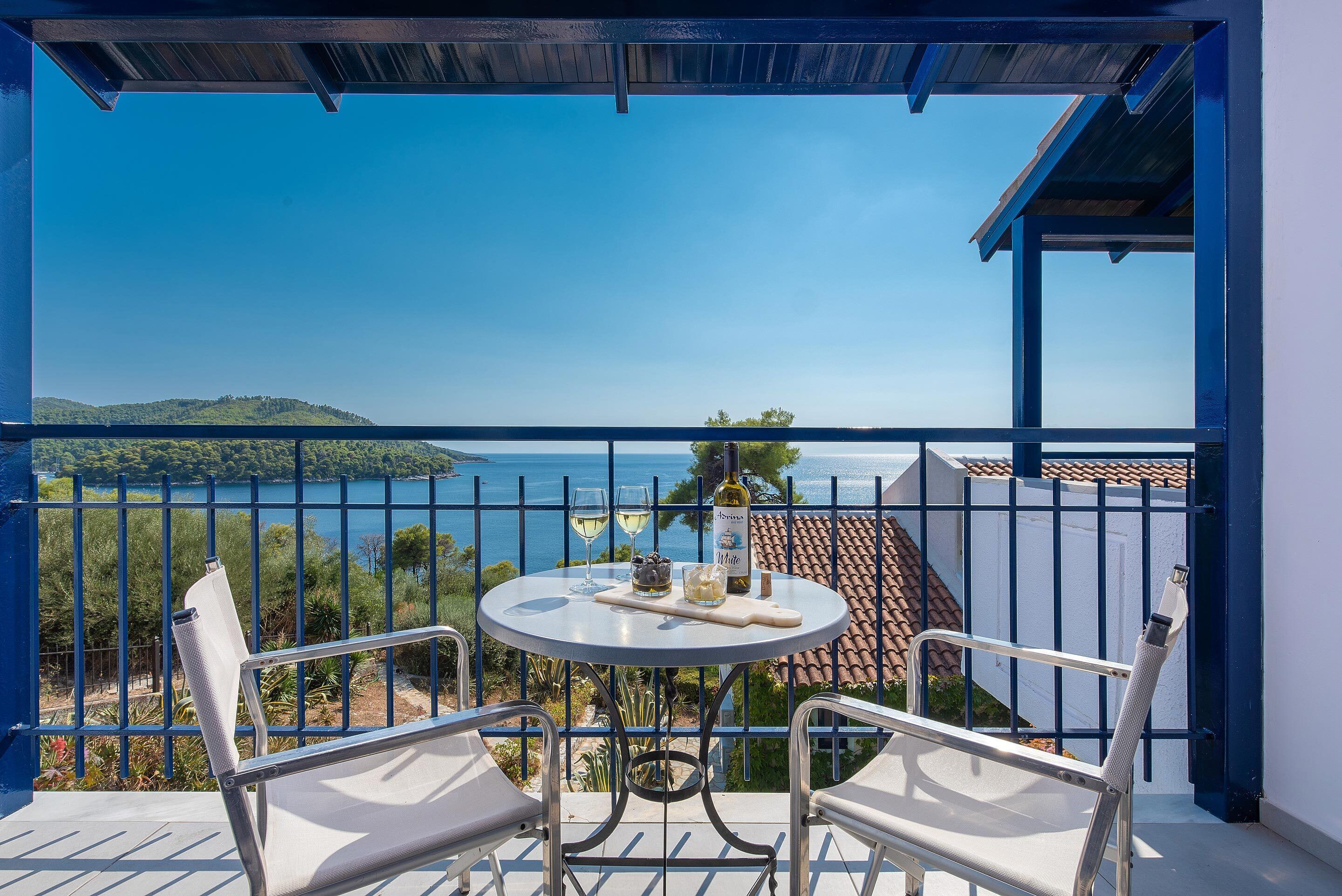 Un balcón con una mesa dispuesta para dos, con vistas panorámicas al mar y las colinas.