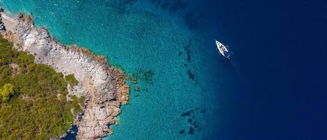 An aerial view of a coastal area with rocky terrain and clear turquoise waters.