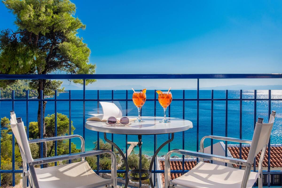 Un balcon avec deux chaises, une table et deux verres de boisson à l’orange.