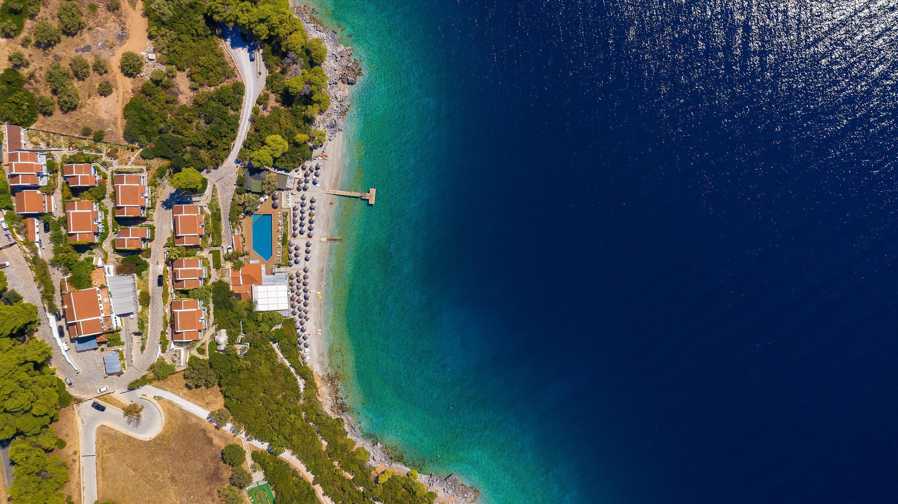 Vista aérea de un complejo turístico costero con villas, una piscina y una playa.