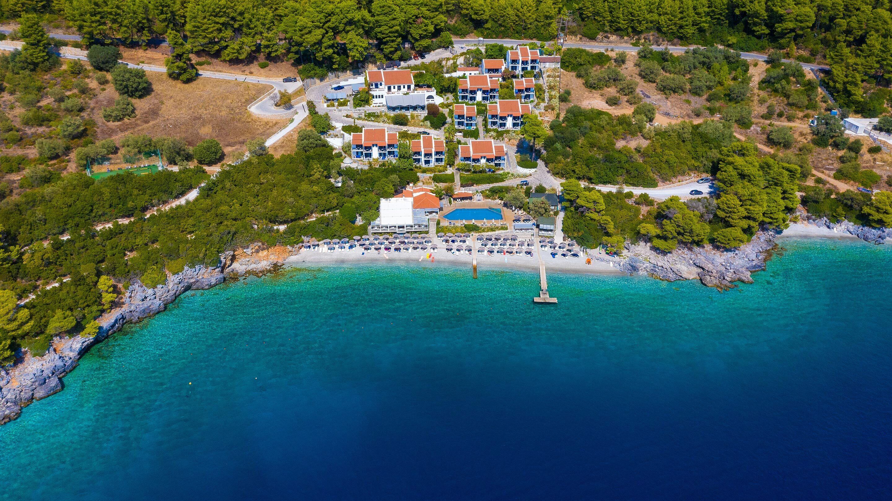 An aerial view of a coastal resort with multiple buildings, a beach, and clear turquoise waters.