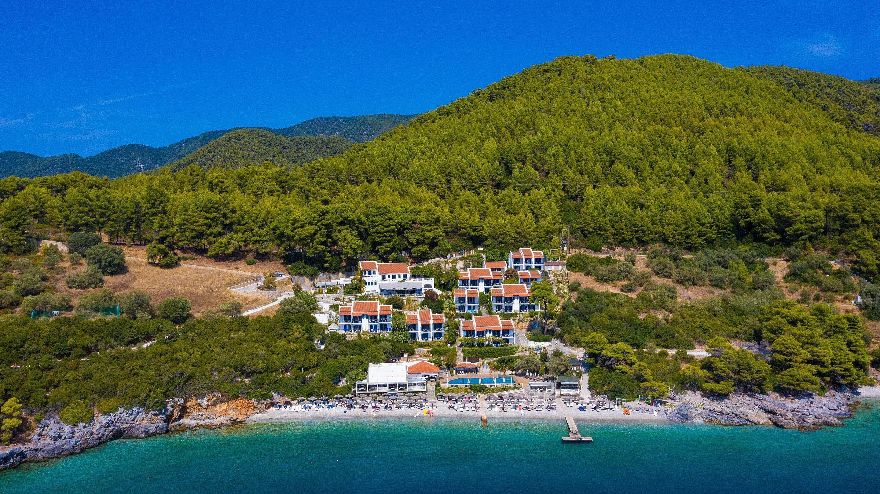 A coastal hotel with multiple buildings, a beach, and a mountainous backdrop.