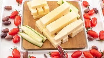 Una tabla de madera con bloques de queso y rodajas de pepino, rodeada de tomates cherry rojos y aceitunas.
