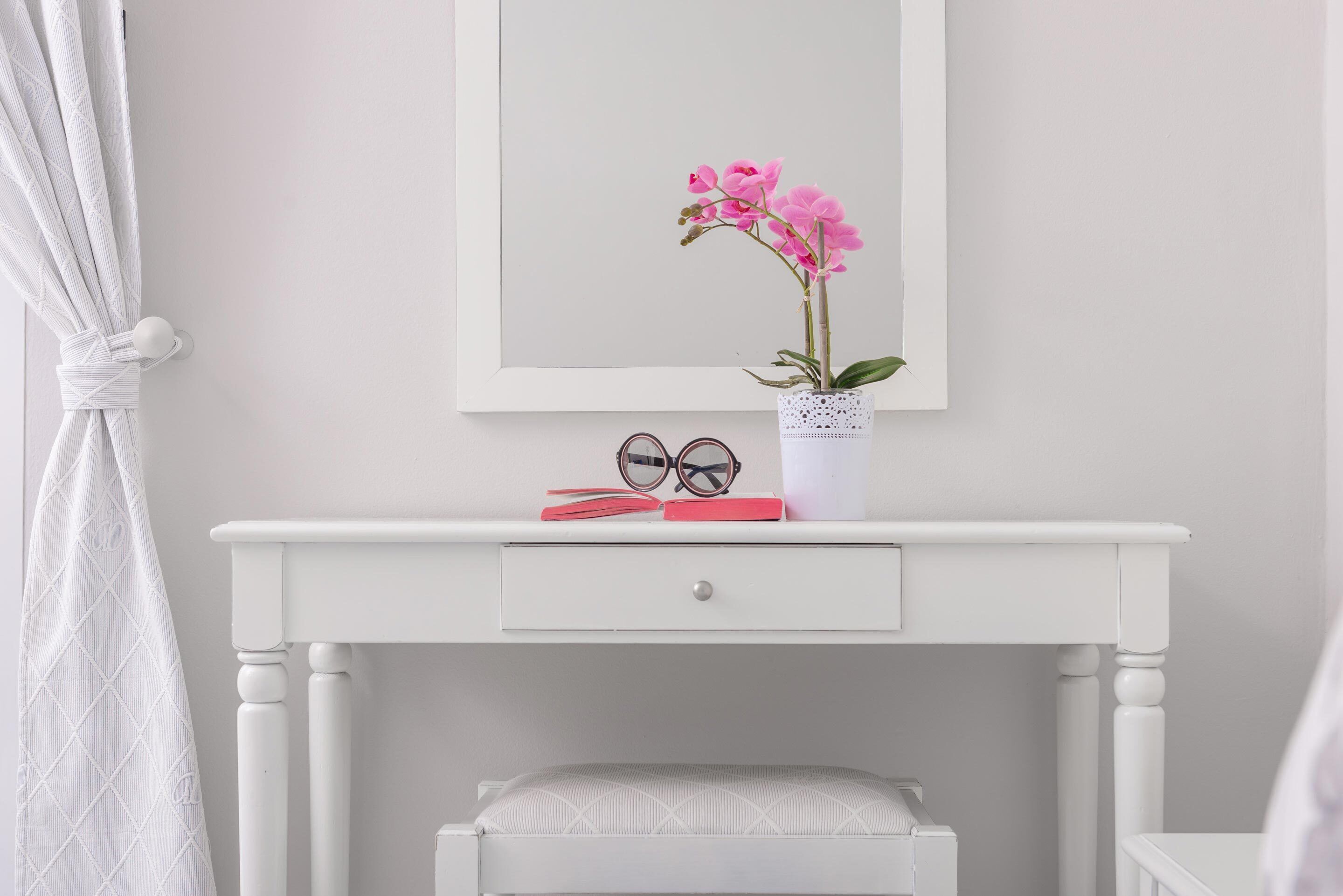 A white desk with a drawer, a potted orchid, and a pair of glasses on top.