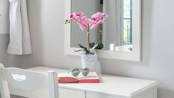 A white desk with a mirror, a vase with pink flowers, a book, and a pair of glasses.